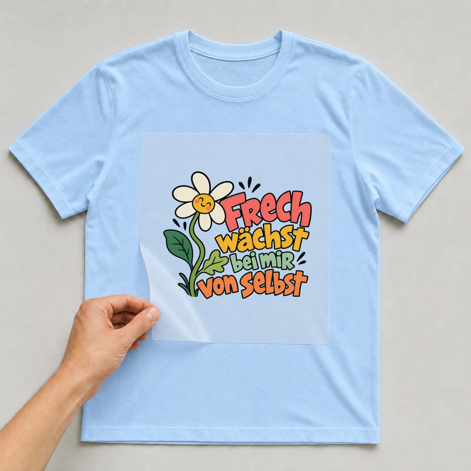 Bügelbild „Frech wächst bei mir von selbst“ auf hellblauem T-Shirt, Folie wird aufgelegt