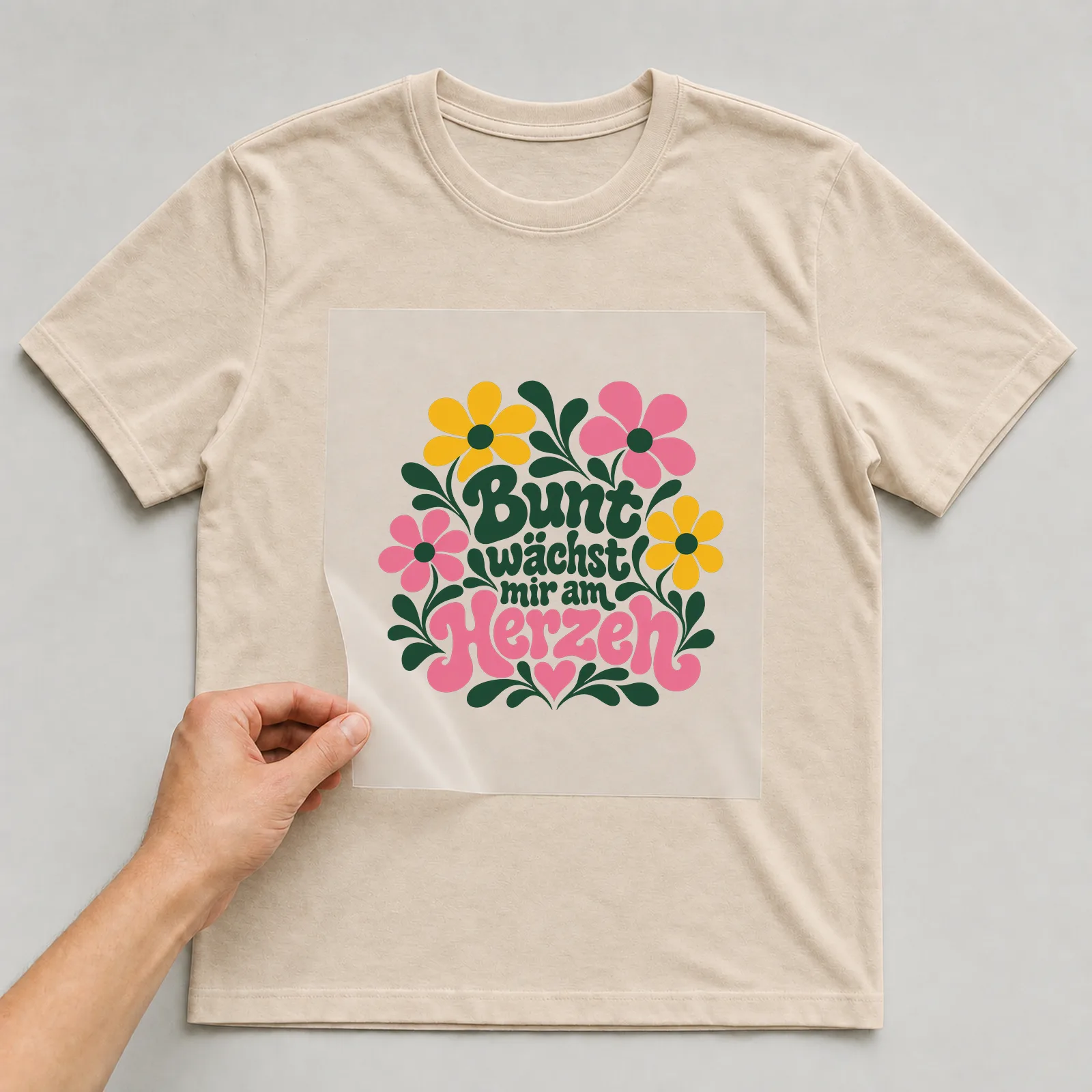 Bügelbild „Bunt wächst mir am Herzen“ auf beigem T-Shirt, Folie wird aufgelegt