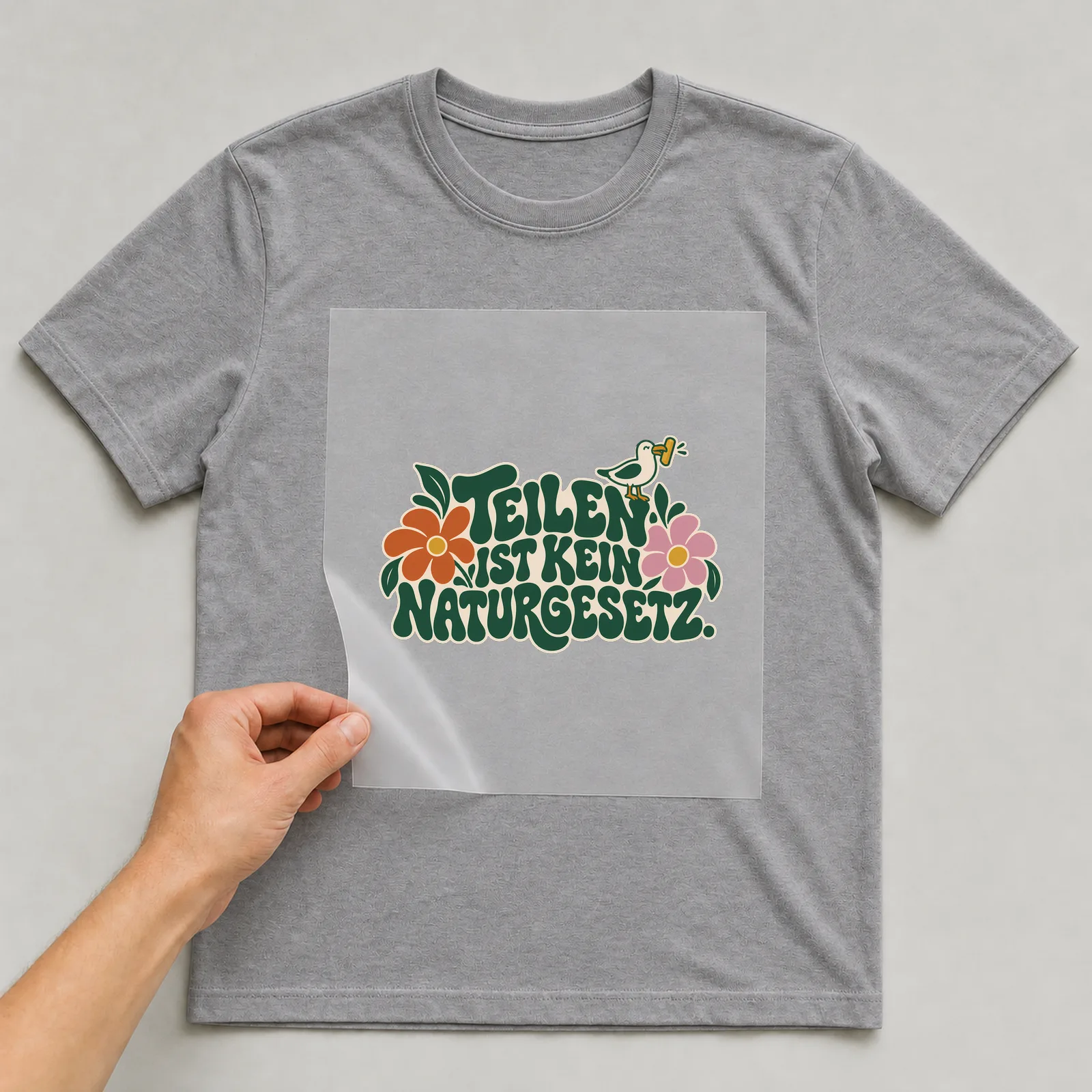 Bügelbild „Teilen ist kein Naturgesetz“ auf grauem T-Shirt, Folie wird aufgelegt