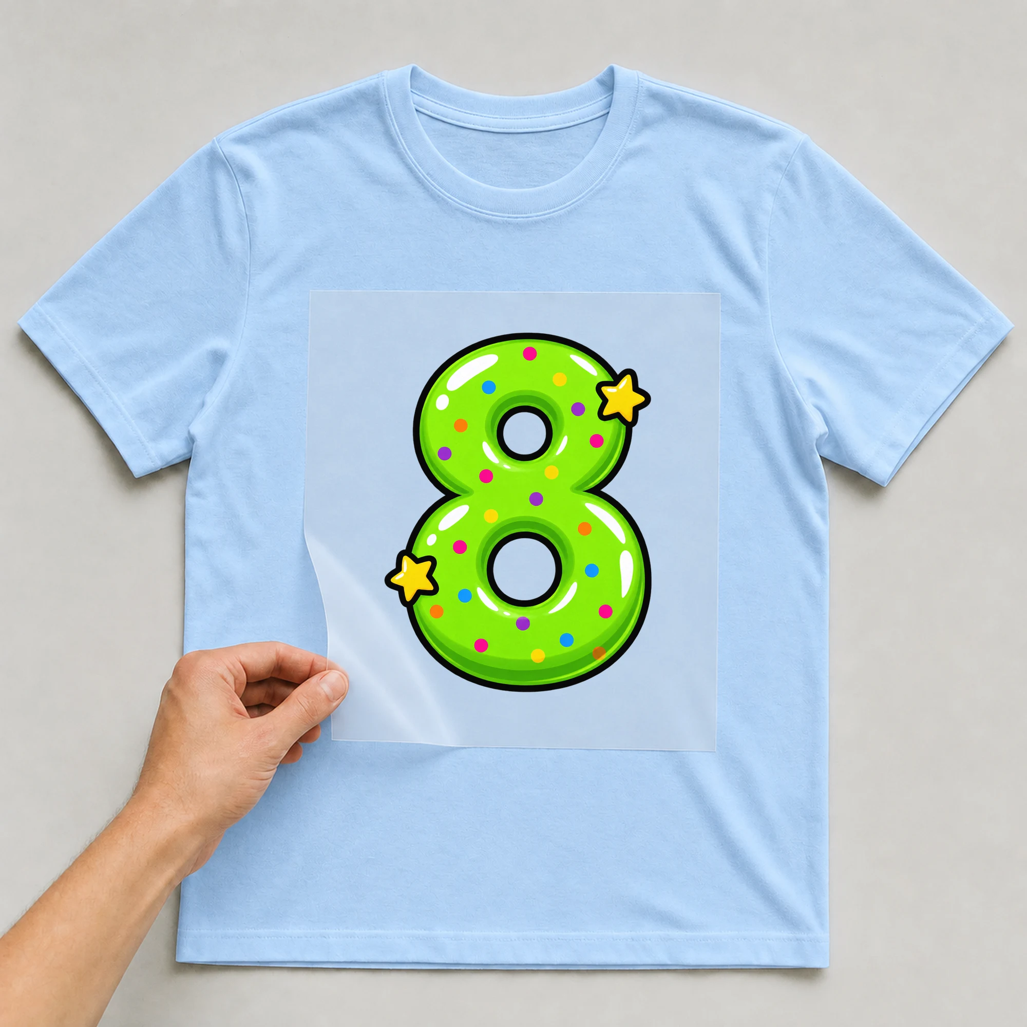 Bügelbild „Zahl 8 im Comic-Ballon-Stil“ auf babyblauem T-Shirt, Folie wird aufgelegt