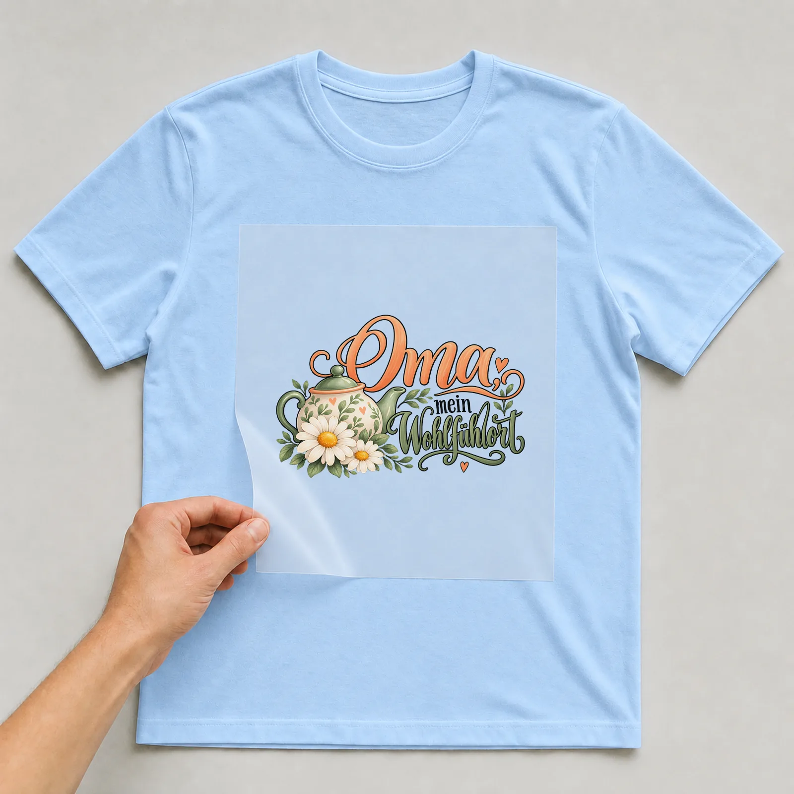 Bügelbild „Oma, mein Wohlfühlort“ auf hellblauem T-Shirt, Folie wird aufgelegt