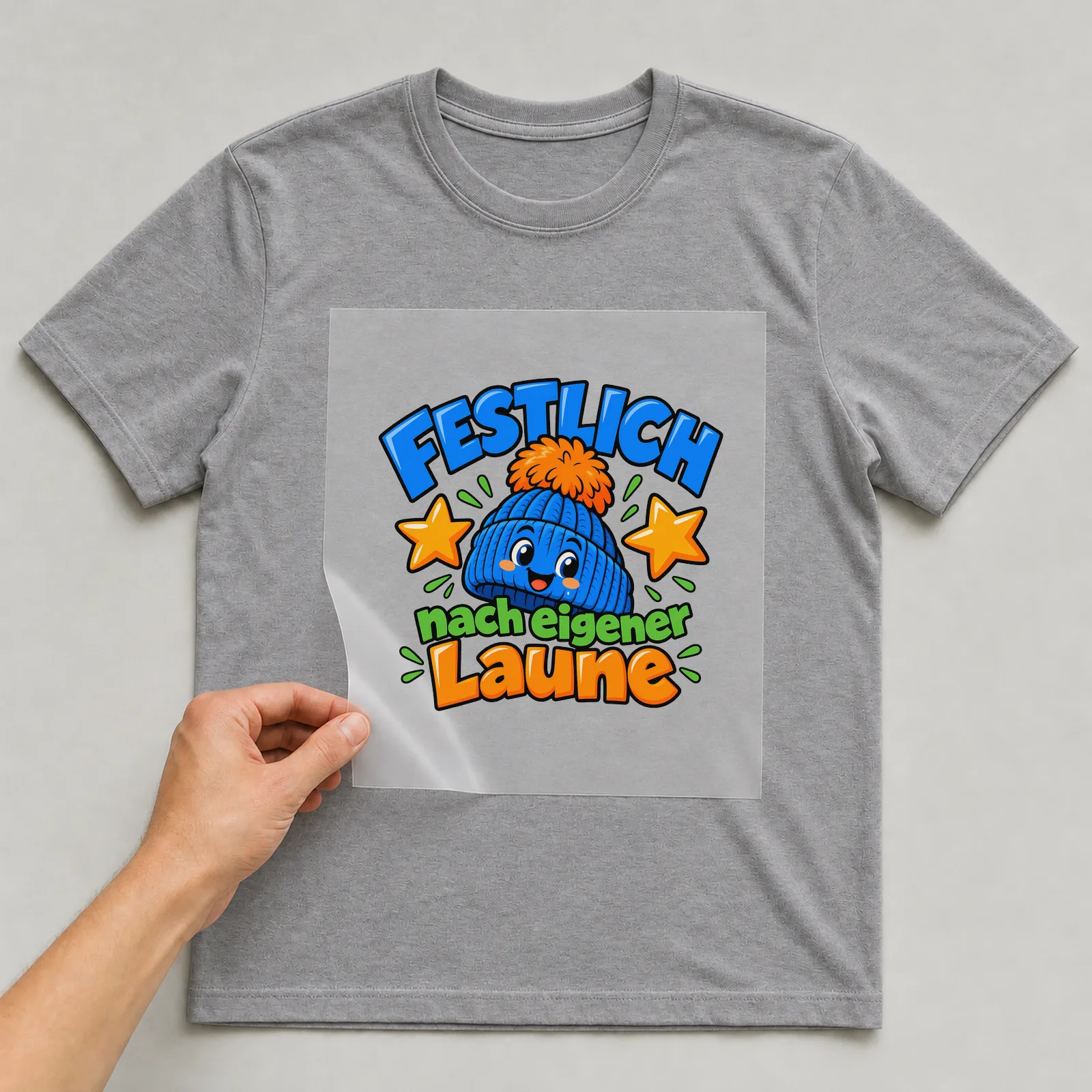 Bügelbild „Festlich nach eigener Laune“ auf grauem T-Shirt, Folie wird aufgelegt