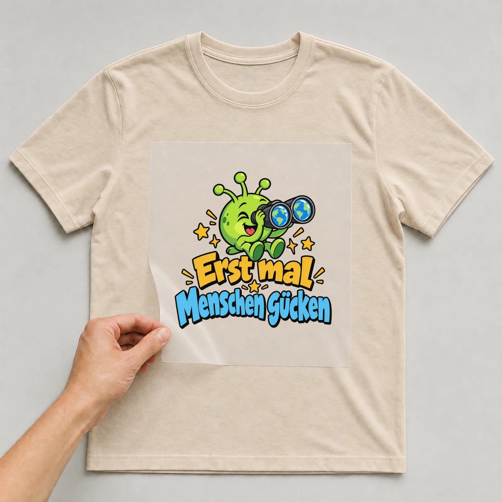 Bügelbild „Erst mal Menschen gucken“ auf beigem T-Shirt, Folie wird aufgelegt