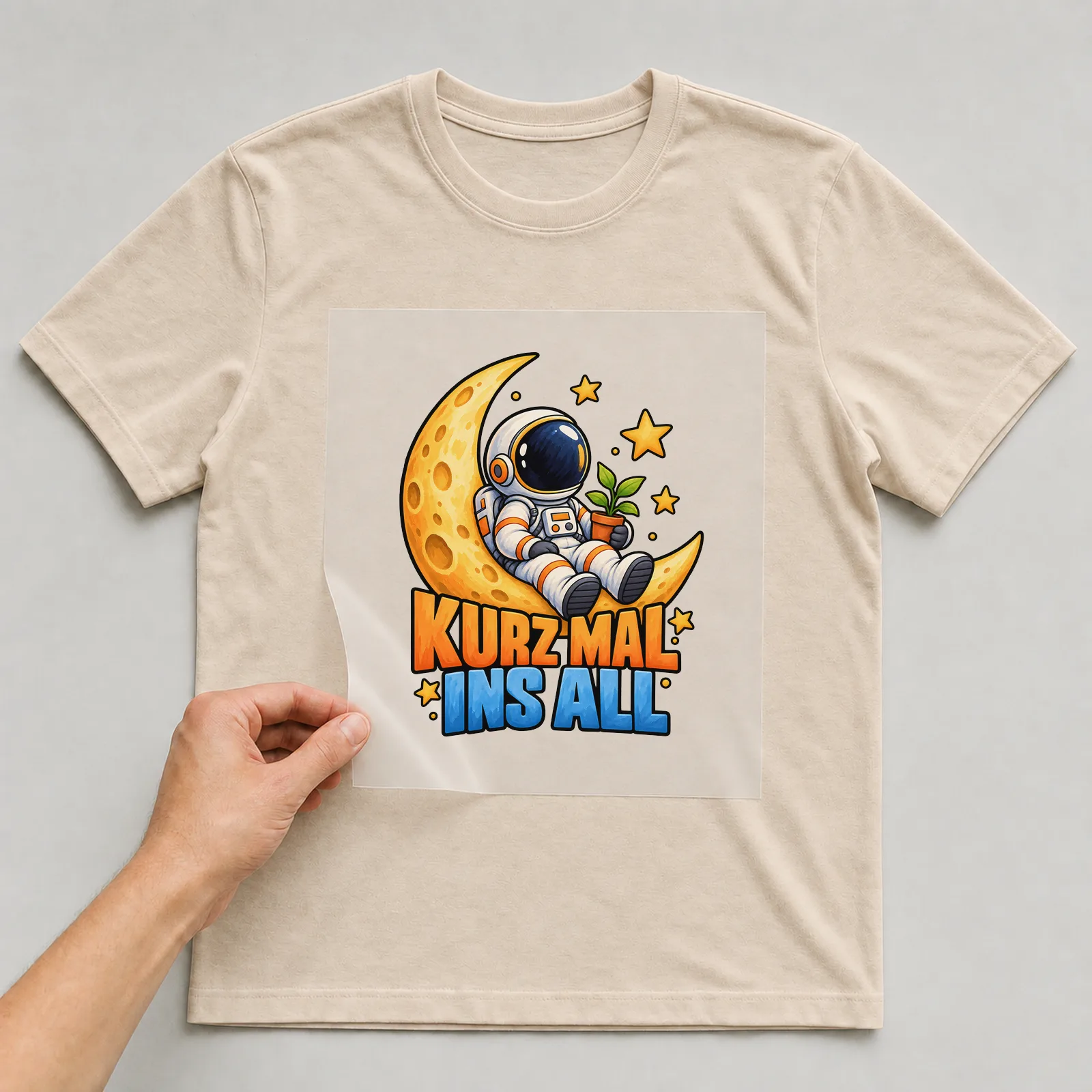 Bügelbild „Kurz mal ins All“ auf beigem T-Shirt, Folie wird aufgelegt