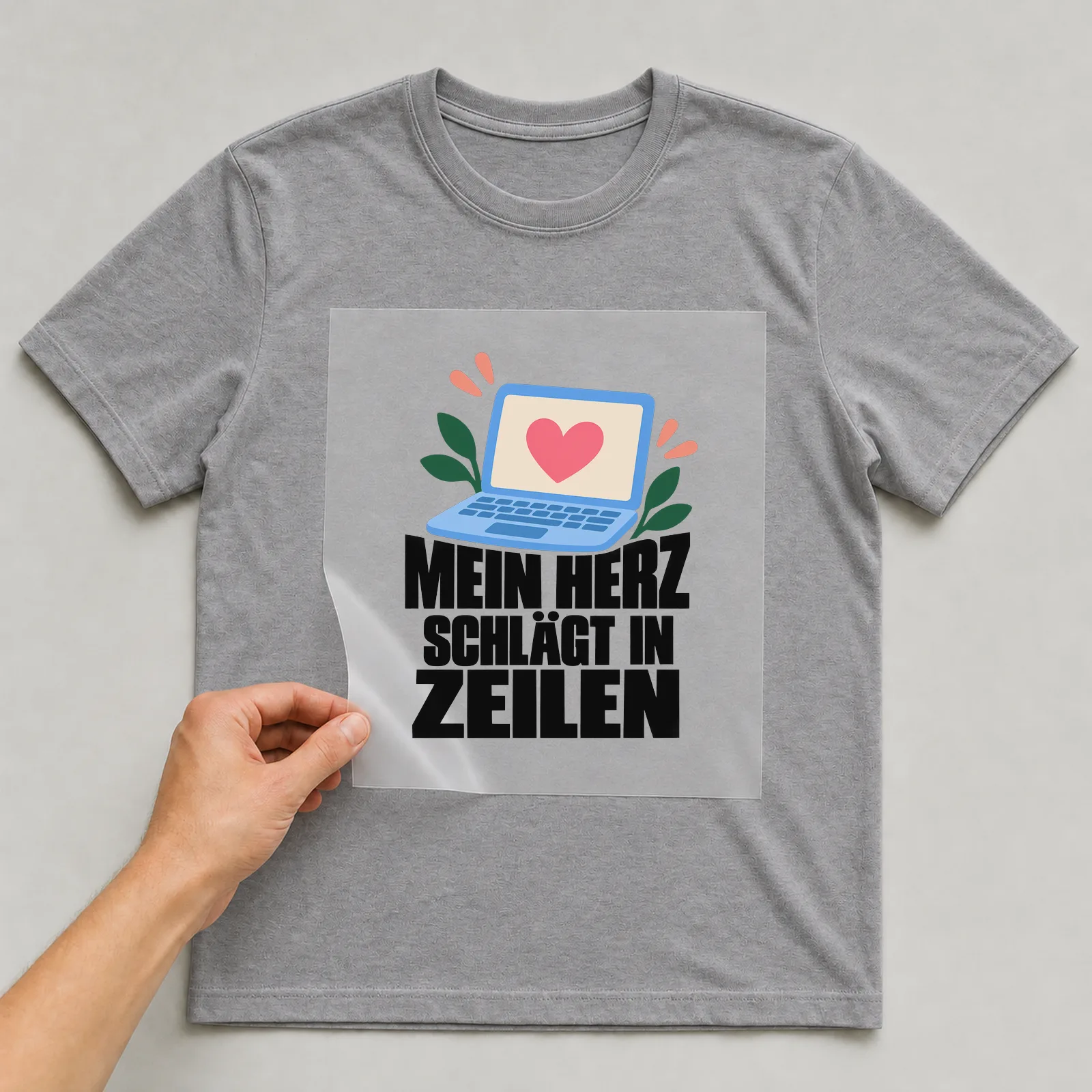 Bügelbild „Mein Herz schlägt in Zeilen“ auf grauem T-Shirt, Folie wird aufgelegt