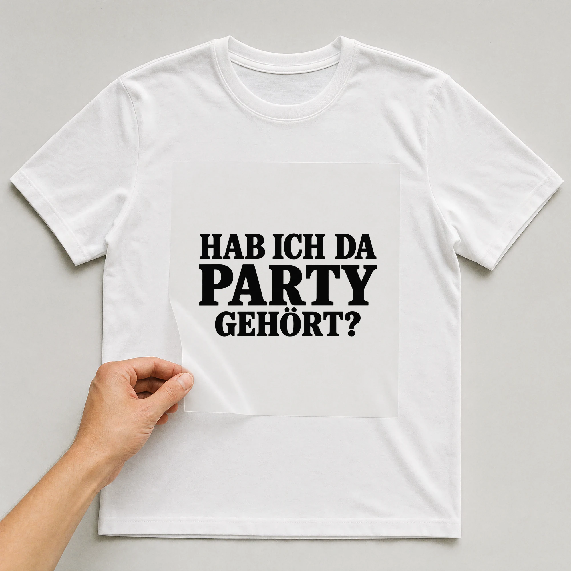 Bügelbild „Hab ich da Party gehört?“ auf weißem T-Shirt, Folie wird aufgelegt