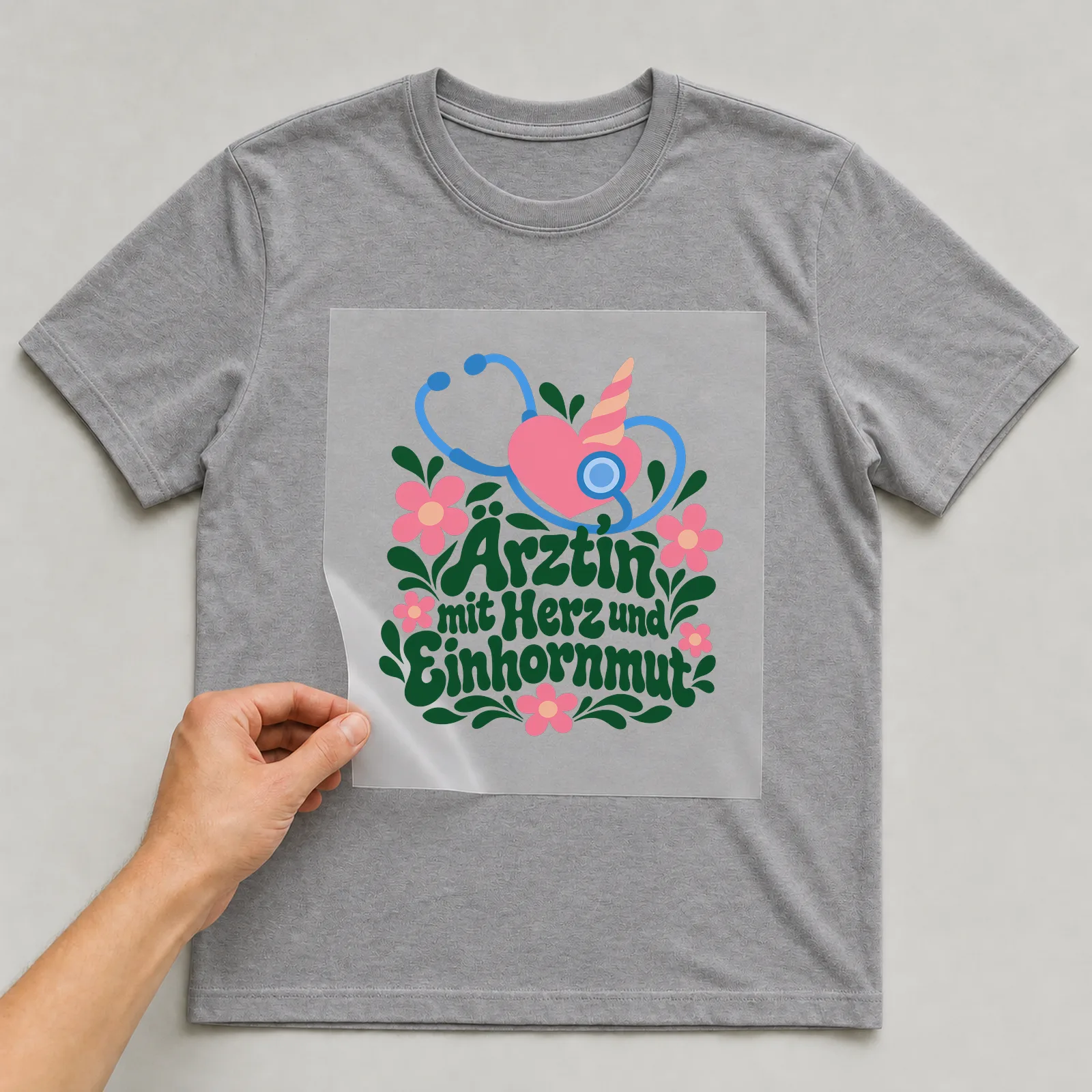 Bügelbild „Ärztin mit Herz und Einhornmut“ auf grauem T-Shirt, Folie wird aufgelegt