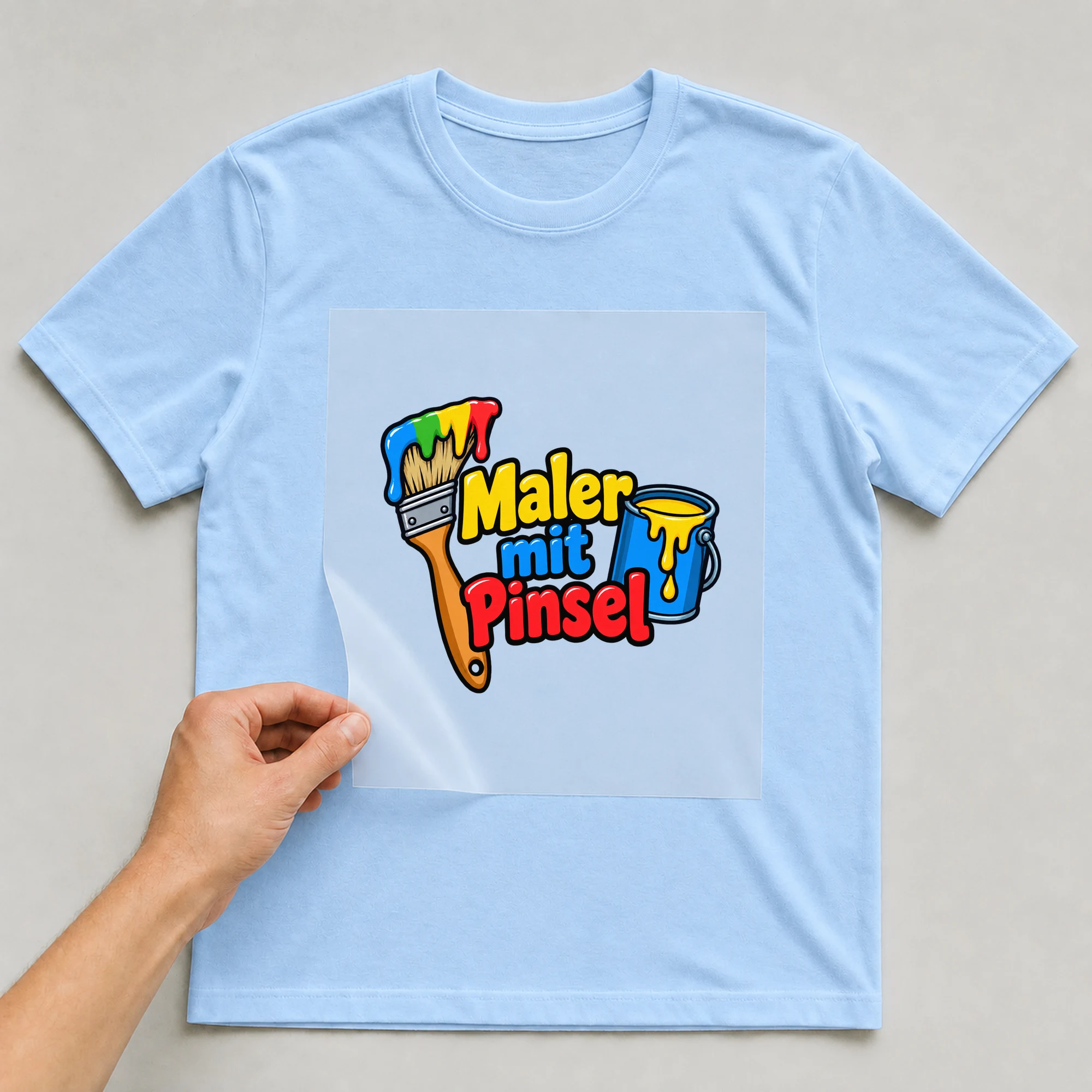 Bügelbild „Maler mit Pinsel“ auf babyblauem T-Shirt, Folie wird aufgelegt