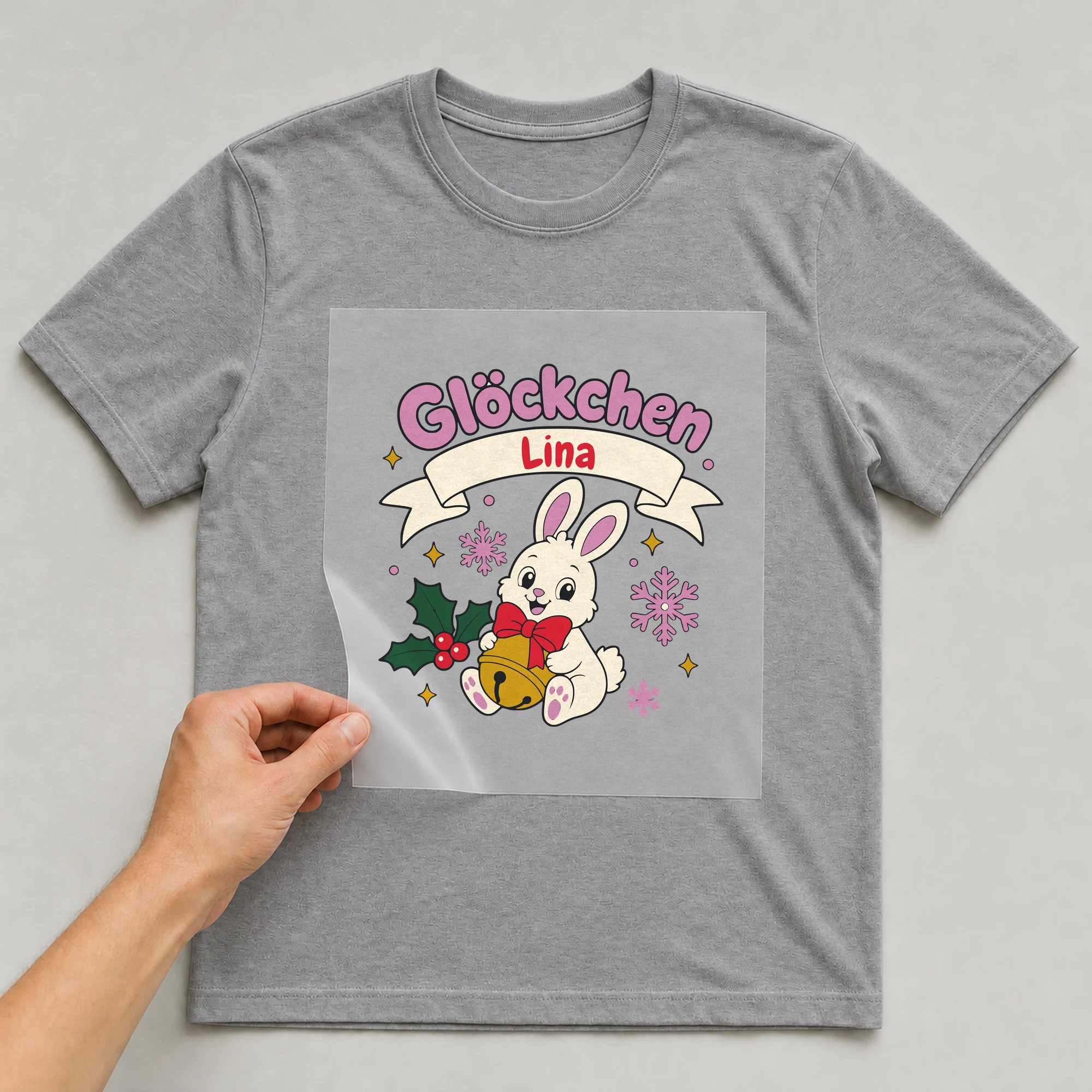 Bügelbild Glöckchen mit Name auf grauem T-Shirt, Folie wird aufgelegt