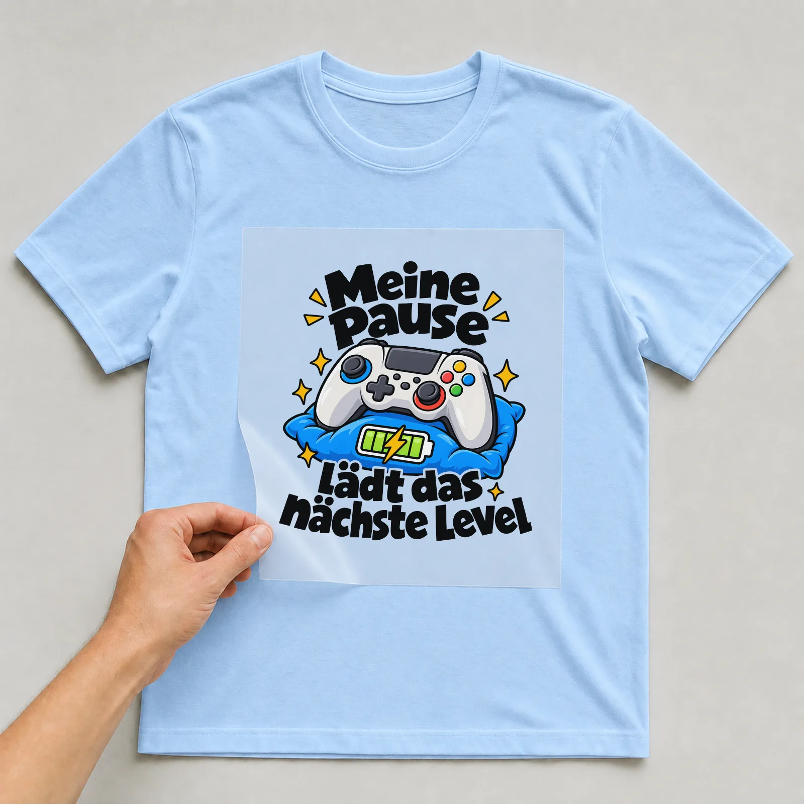 Bügelbild „Meine Pause lädt das nächste Level“ auf hellblauem T-Shirt, Folie wird aufgelegt