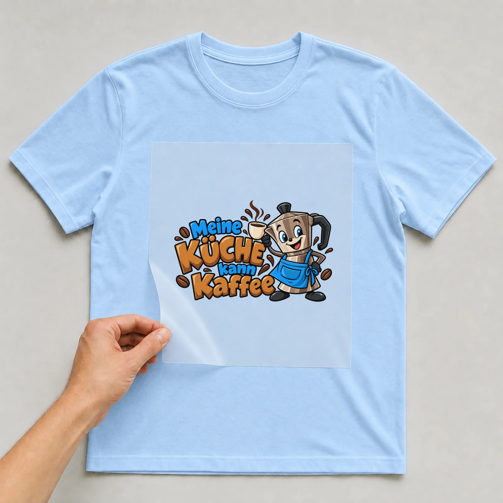 Bügelbild „Meine Küche kann Kaffee“ auf hellblauem T-Shirt, Folie wird aufgelegt