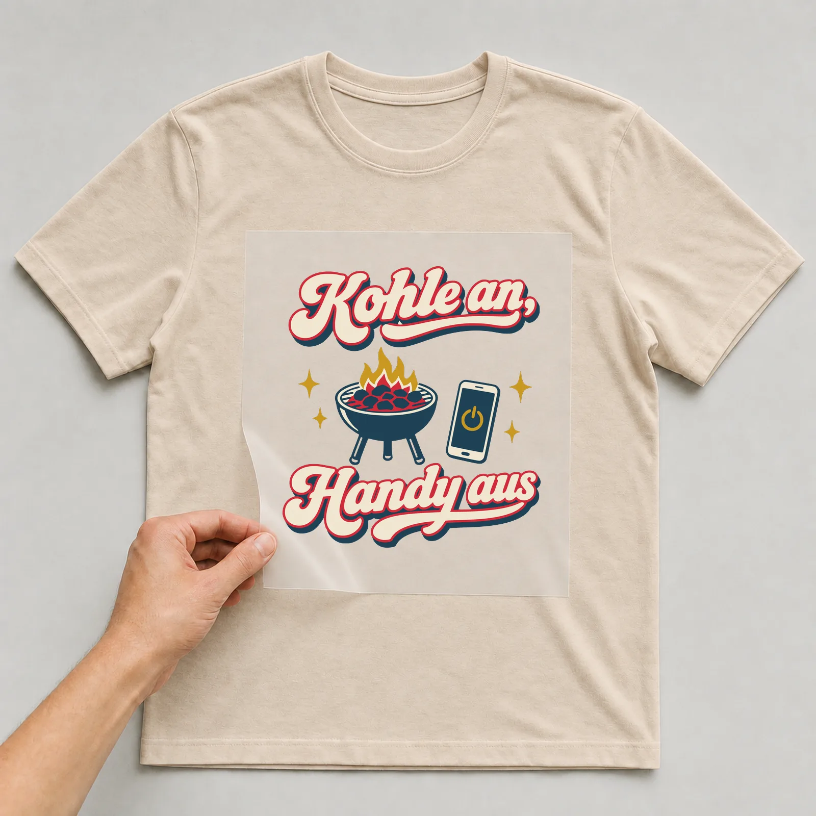 Bügelbild Kohle an, Handy aus auf beigem T-Shirt, Folie wird aufgelegt