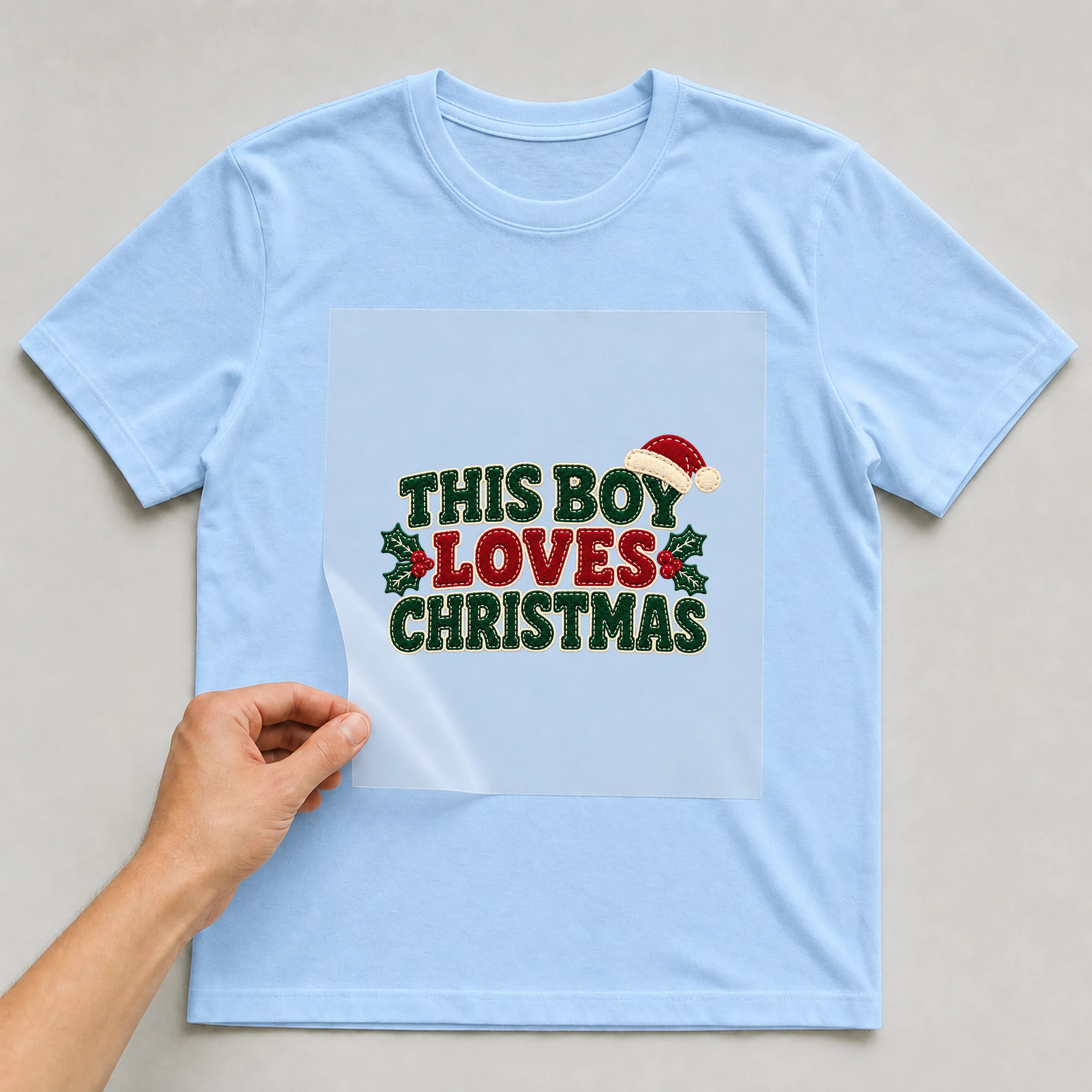 Bügelbild „This Boy Loves Christmas“ auf babyblauem T-Shirt, Folie wird aufgelegt