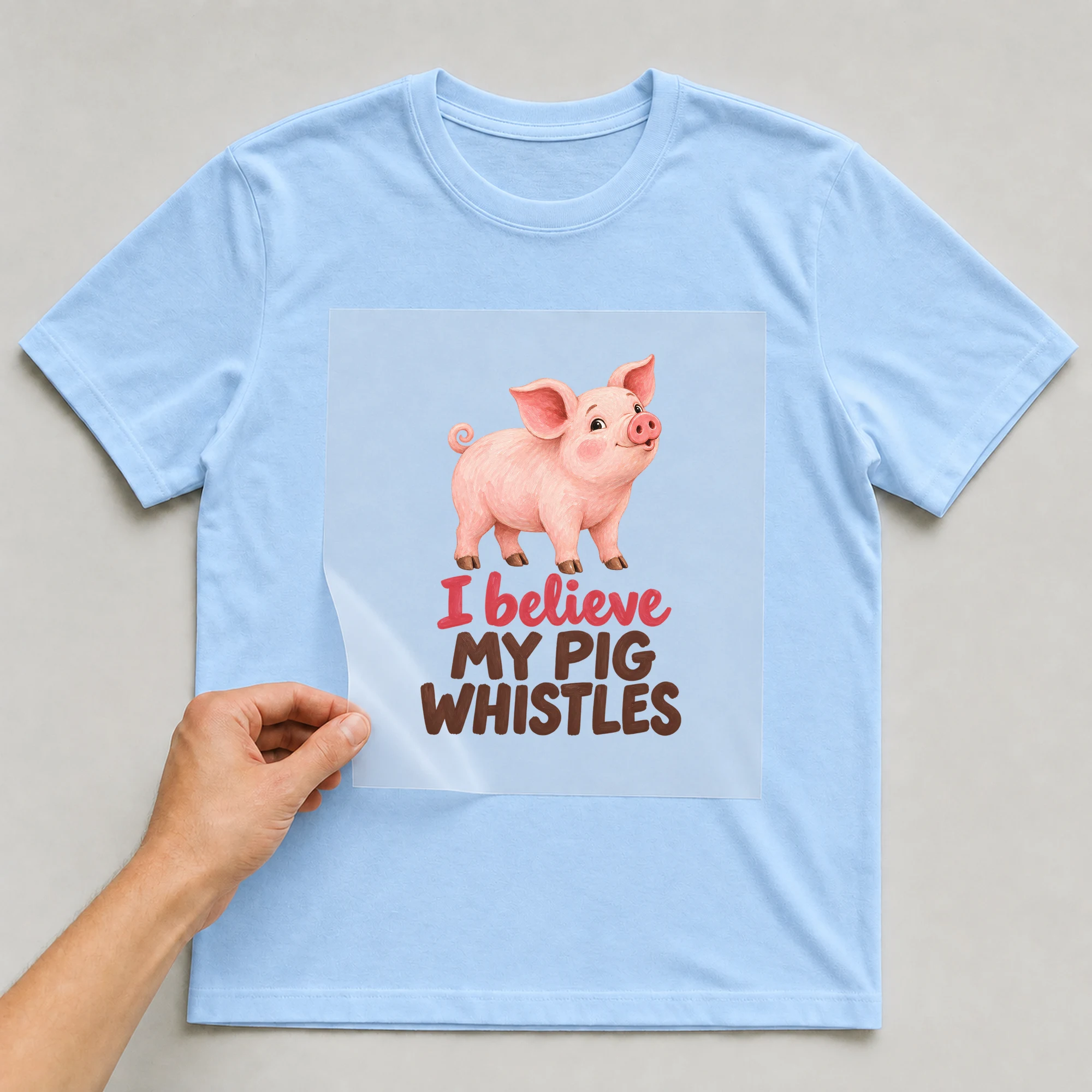 Bügelbild „I Believe My Pig Whistles“ auf babyblauem T-Shirt, Folie wird aufgelegt