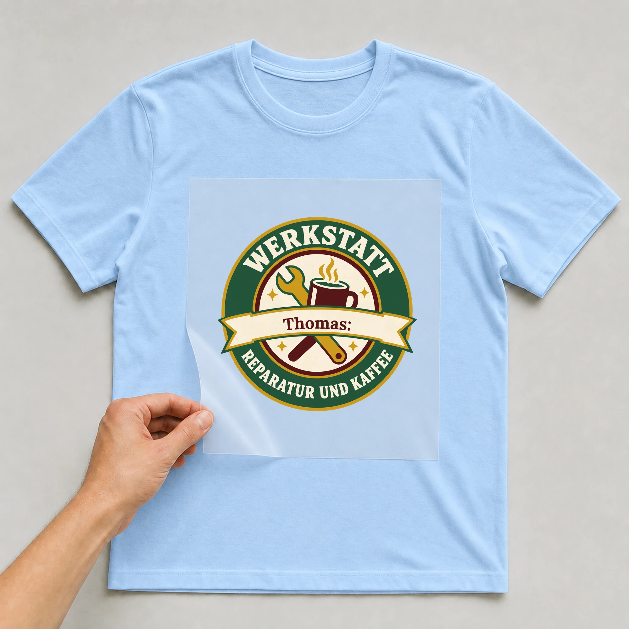 Bügelbild Werkstatt: Reparatur und Kaffee mit Name auf hellblauem T-Shirt, Folie wird aufgelegt