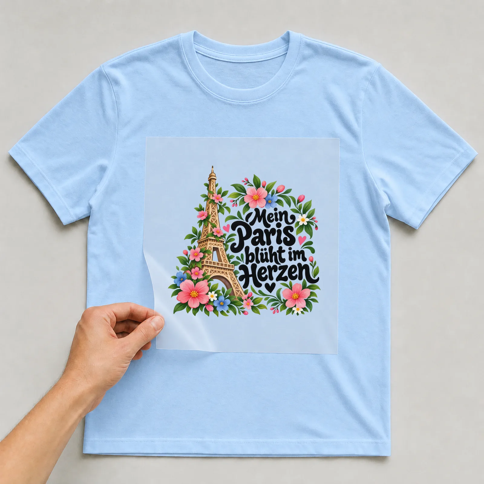 Bügelbild „Mein Paris blüht im Herzen“ auf hellblauem T-Shirt, Folie wird aufgelegt