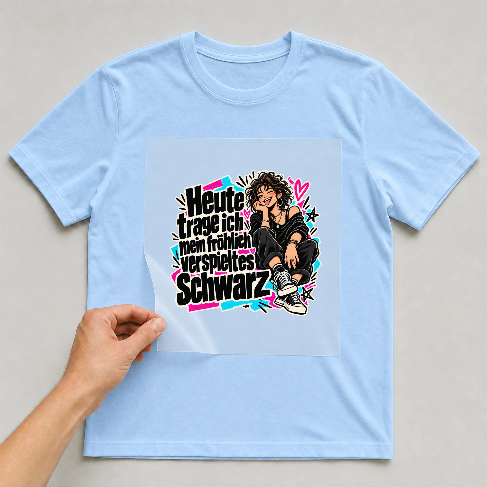 Bügelbild „Heute trage ich mein fröhlich verspieltes Schwarz“ auf babyblauem T-Shirt, Folie wird aufgelegt