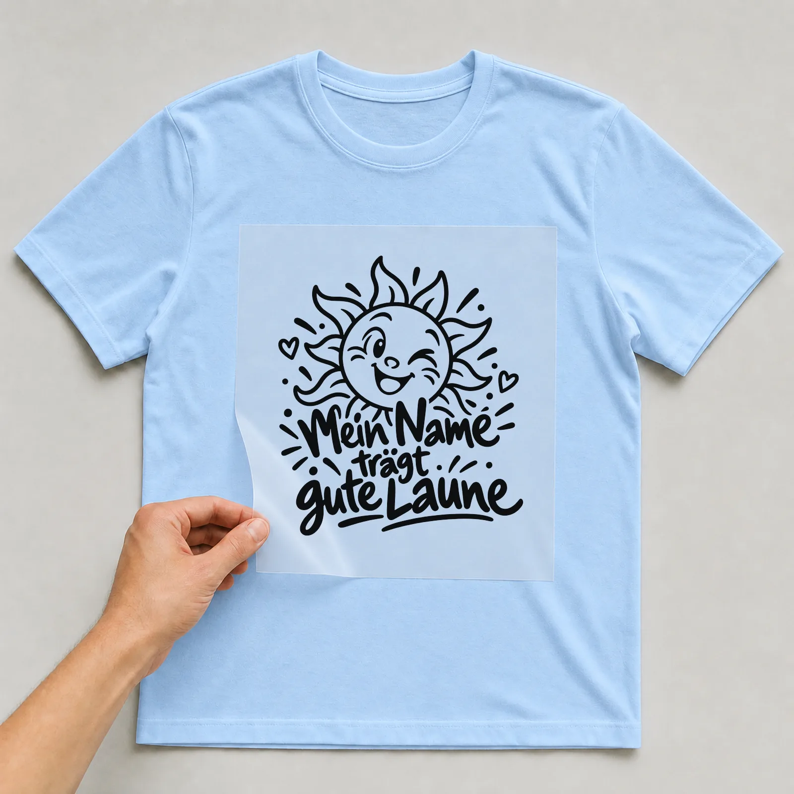 Bügelbild „Mein Name trägt gute Laune“ auf hellblauem T-Shirt, Folie wird aufgelegt