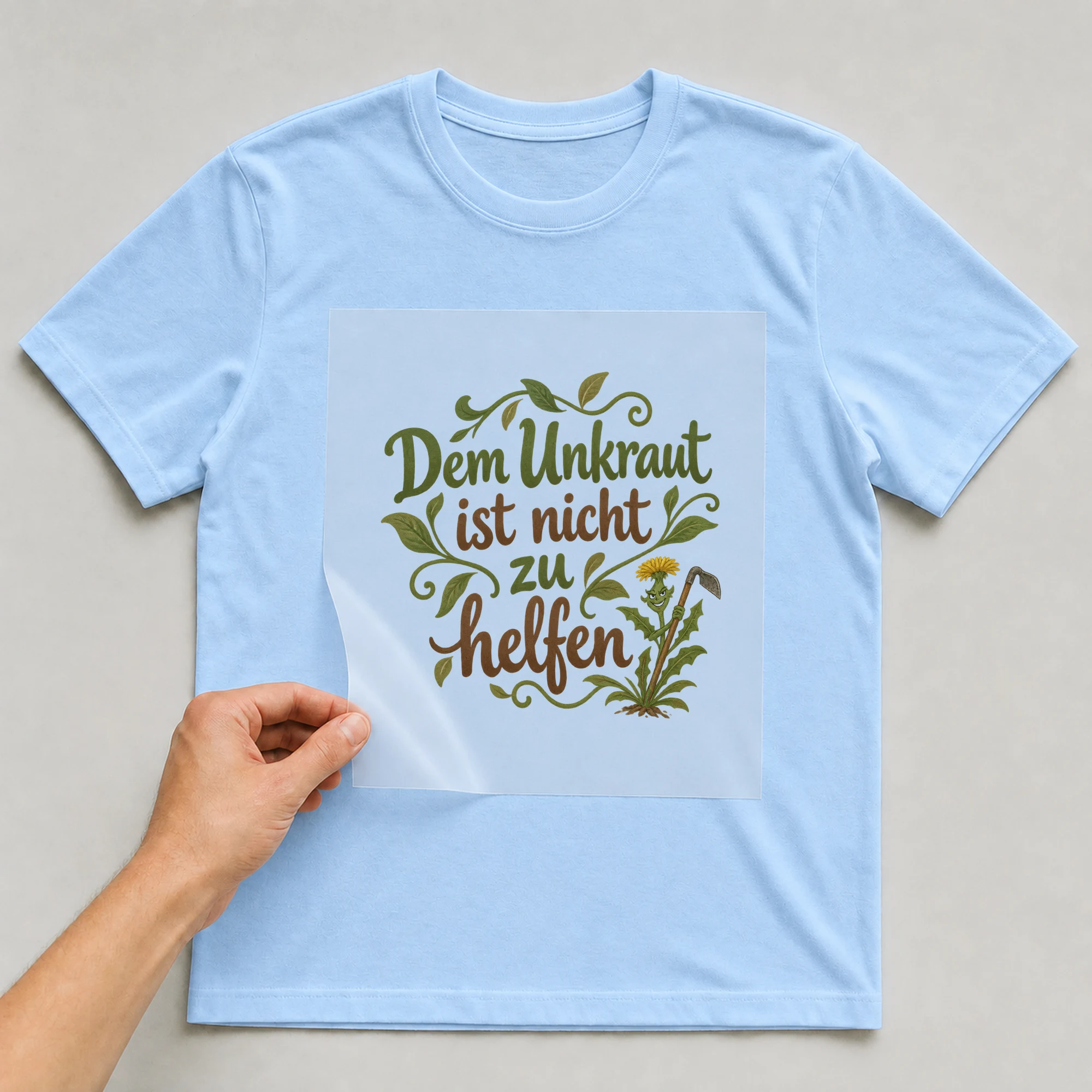 Bügelbild „Dem Unkraut ist nicht zu helfen“ auf babyblauem T-Shirt, Folie wird aufgelegt