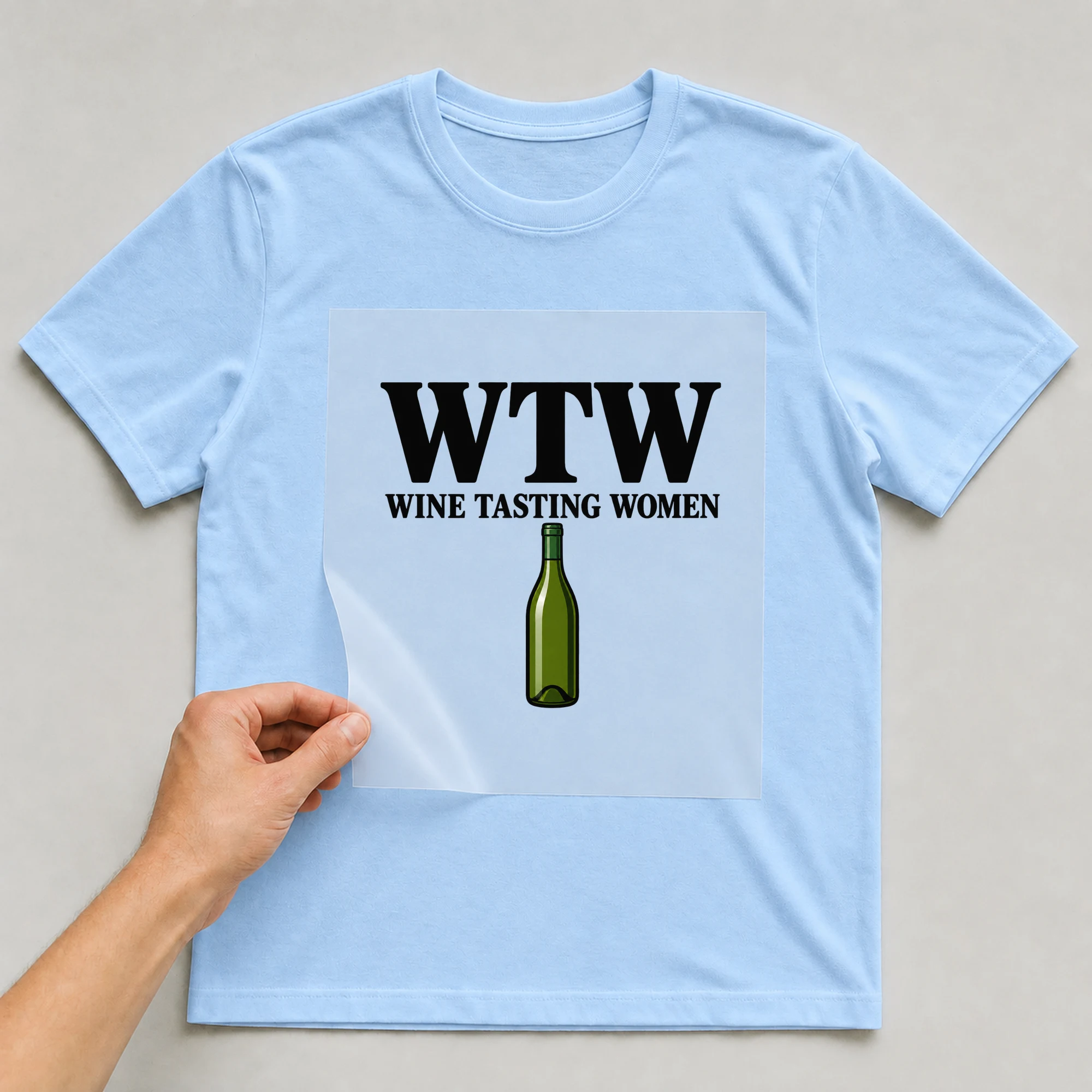 Bügelbild „WTW: Wine Tasting Women“ auf babyblauem T-Shirt, Folie wird aufgelegt