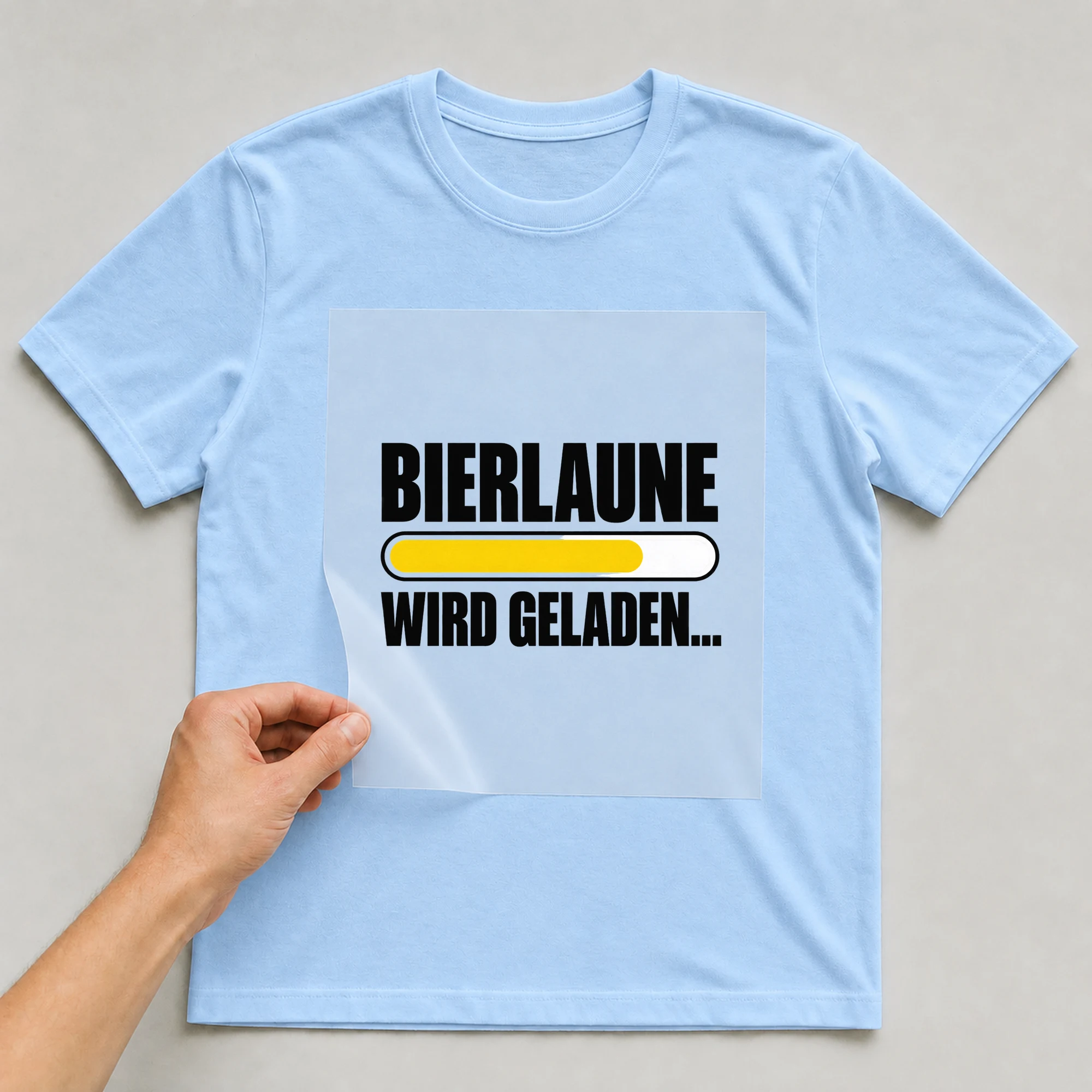 Bügelbild „Bierlaune wird geladen“ auf babyblauem T-Shirt, Folie wird aufgelegt