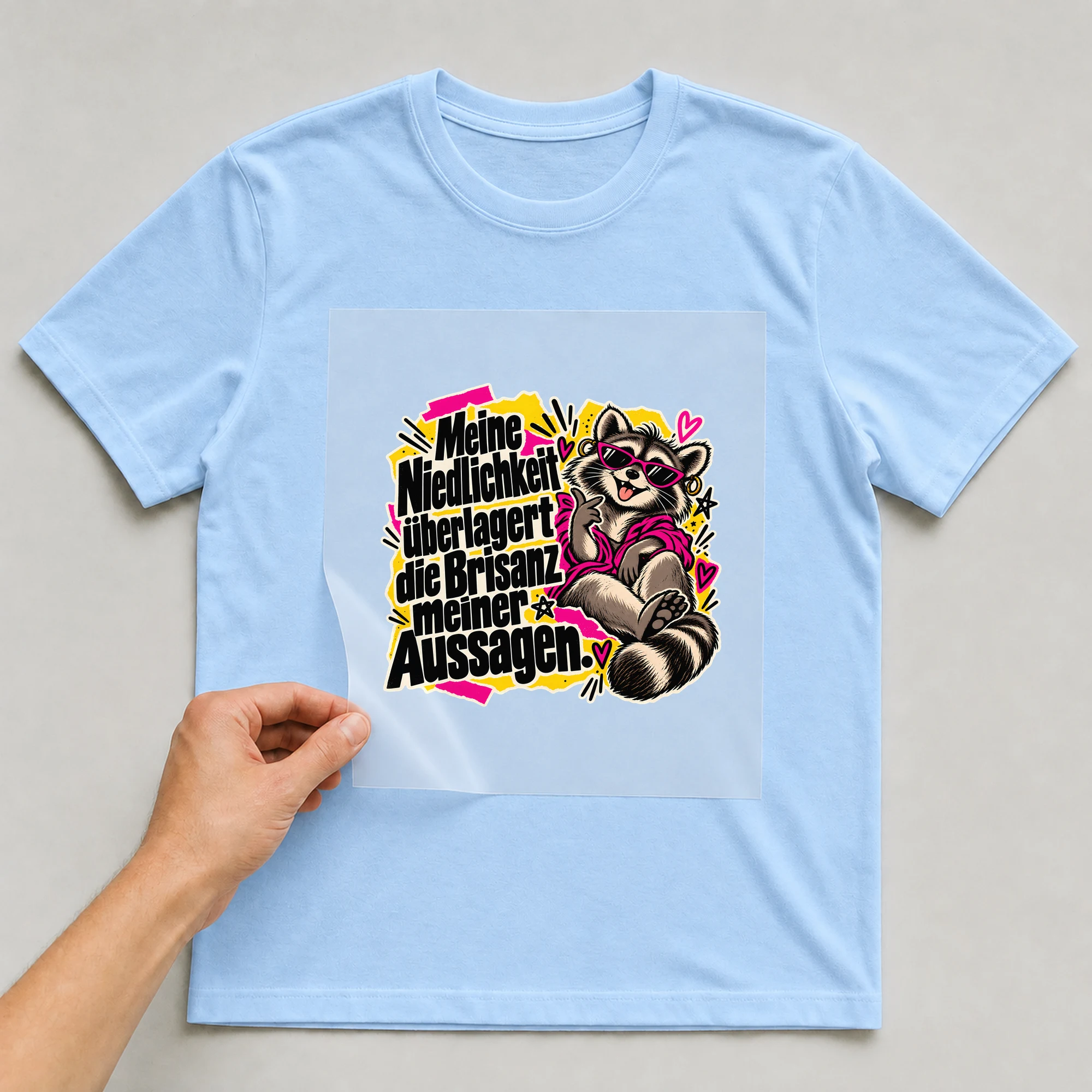 Bügelbild „Meine Niedlichkeit überlagert die Brisanz meiner Aussagen“ auf babyblauem T-Shirt, Folie wird aufgelegt