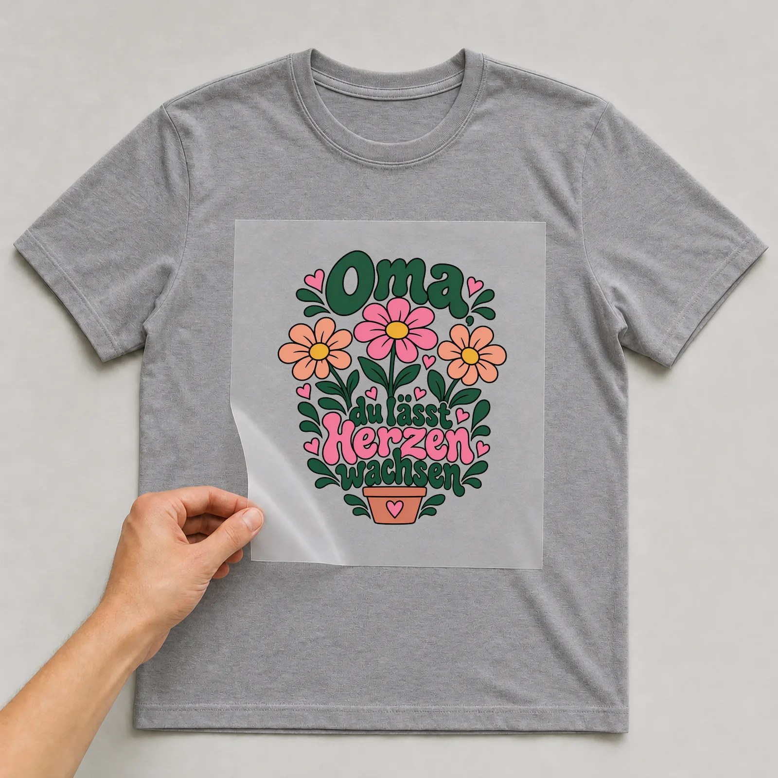 Bügelbild „Oma, du lässt Herzen wachsen“ auf grauem T-Shirt, Folie wird aufgelegt