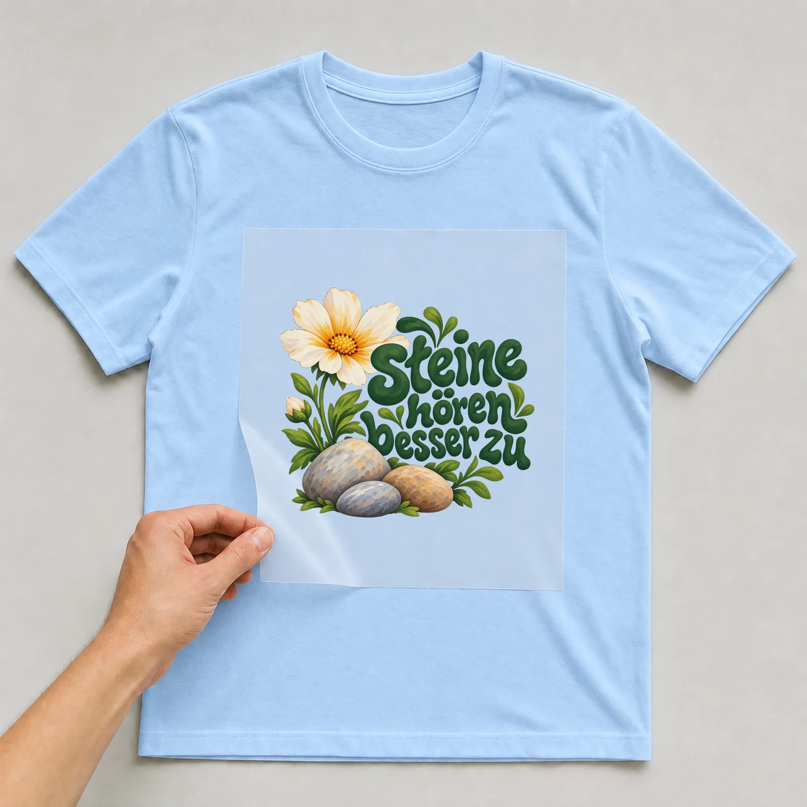 Bügelbild „Steine hören besser zu“ auf hellblauem T-Shirt, Folie wird aufgelegt