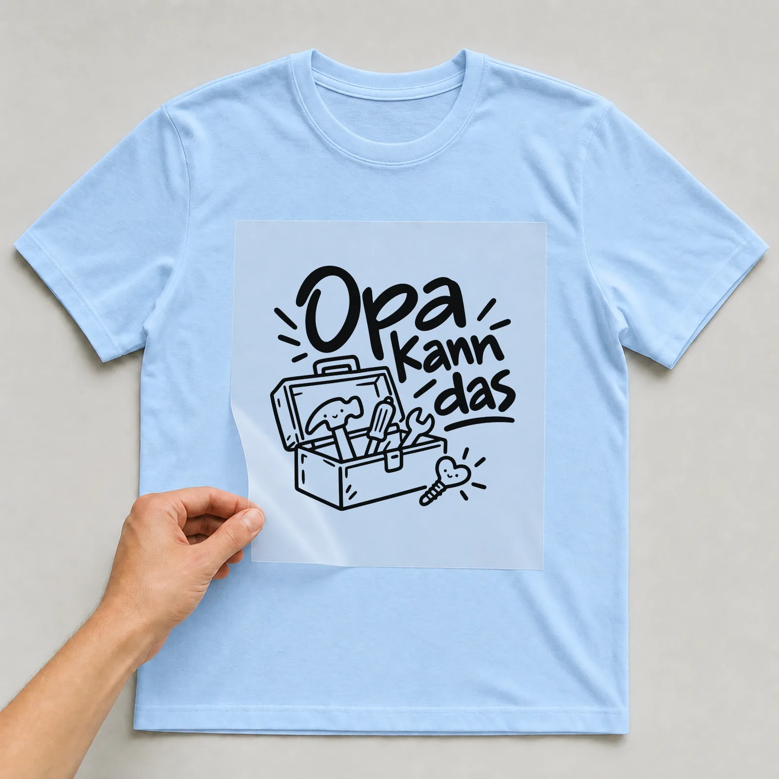 Bügelbild „Opa kann das“ auf hellblauem T-Shirt, Folie wird aufgelegt