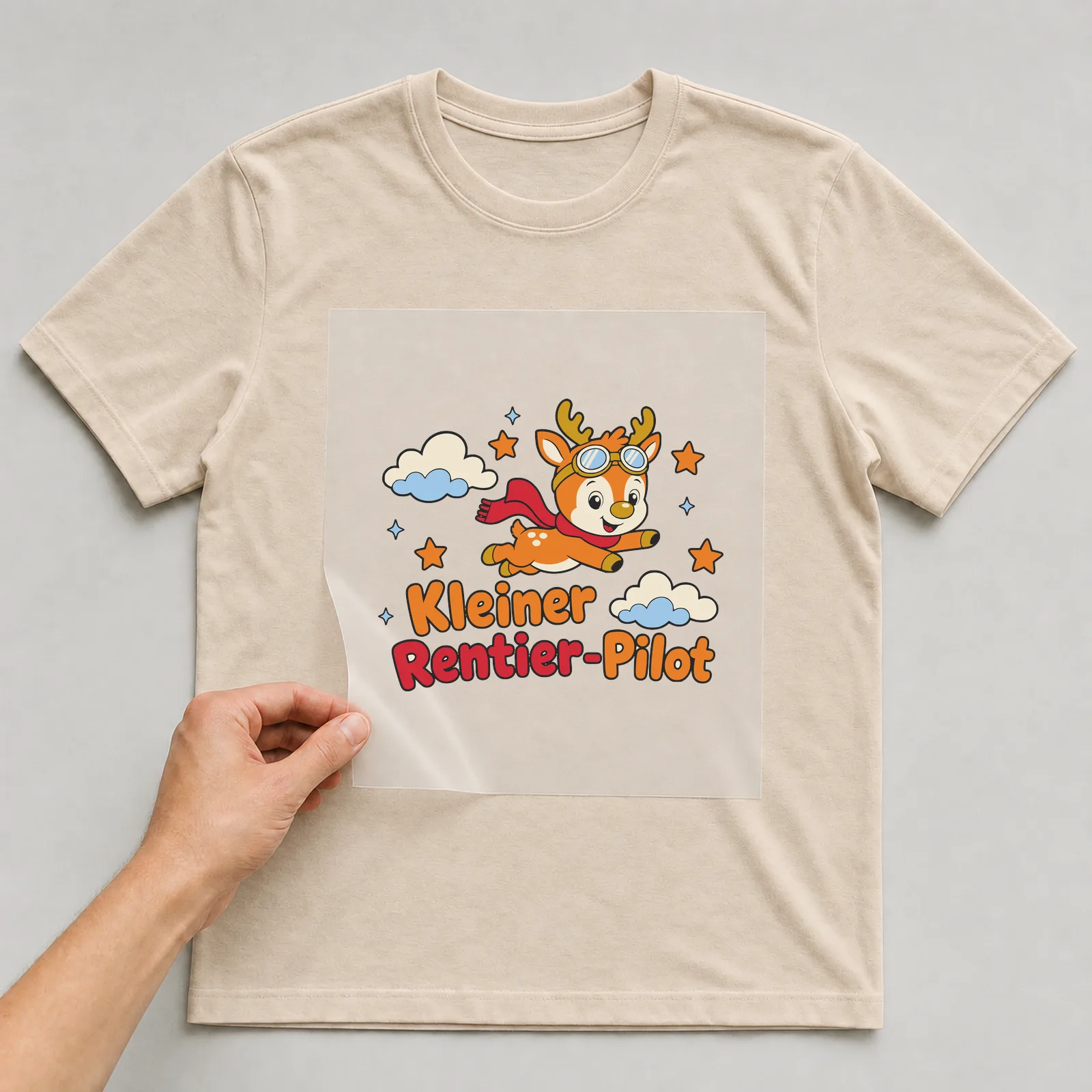 Bügelbild Kleiner Rentier-Pilot auf beigem T-Shirt, Folie wird aufgelegt