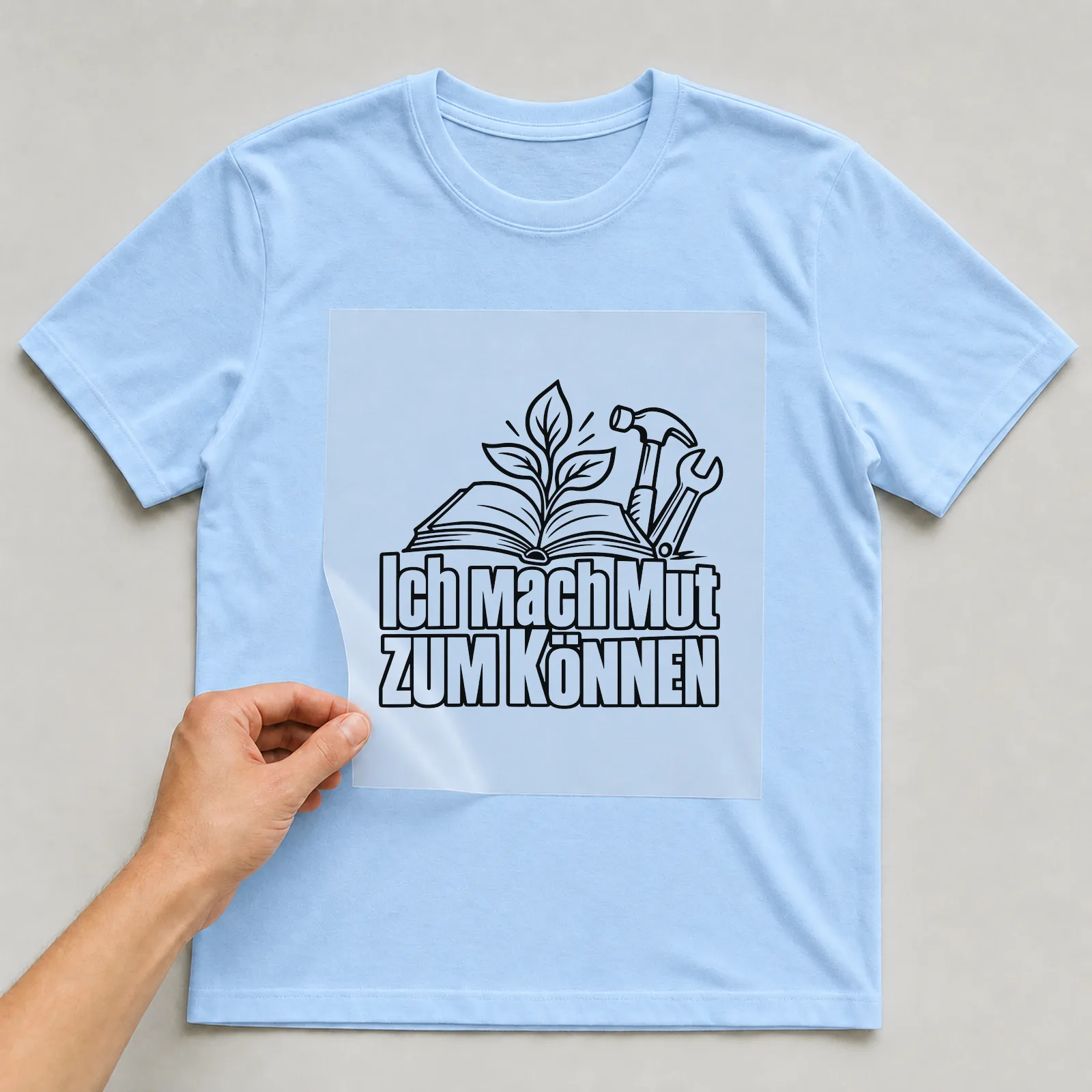 Bügelbild „Ich mach Mut zum können“ auf hellblauem T-Shirt, Folie wird aufgelegt