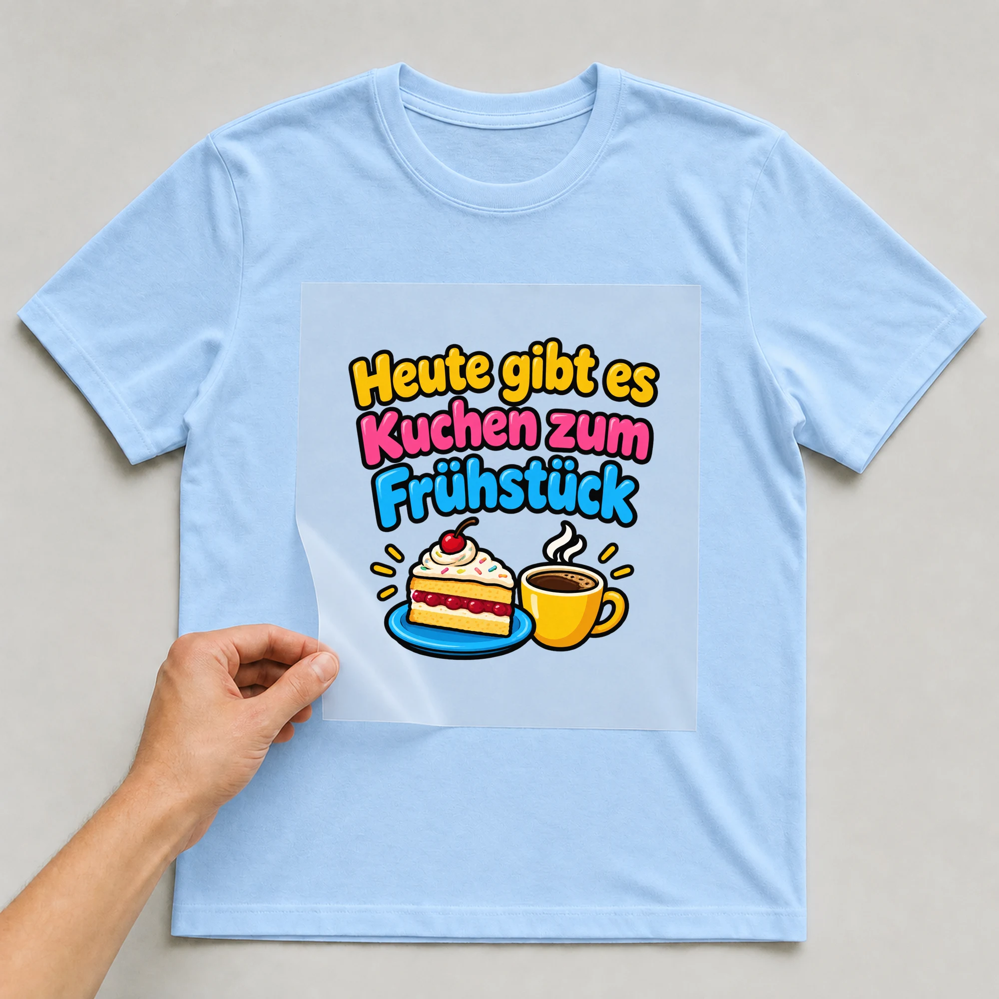 Bügelbild „Heute gibt es kuchen zum fruehstueck“ auf babyblauem T-Shirt, Folie wird aufgelegt