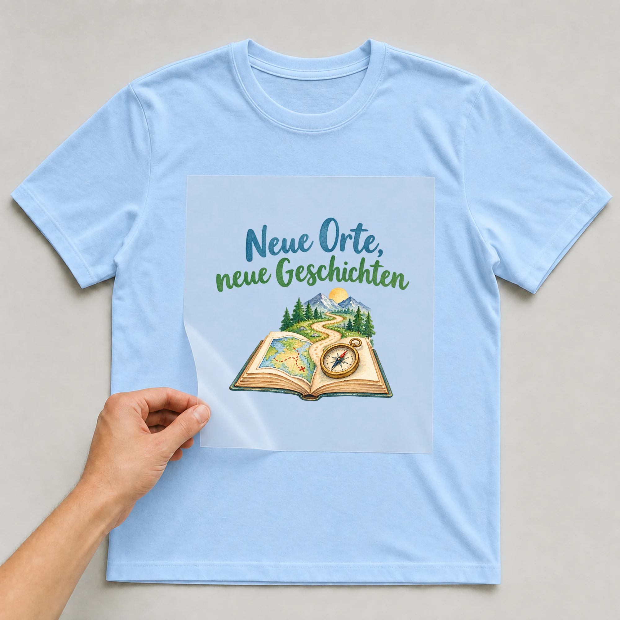 Bügelbild „Neue Orte, neue Geschichten“ auf babyblauem T-Shirt, Folie wird aufgelegt