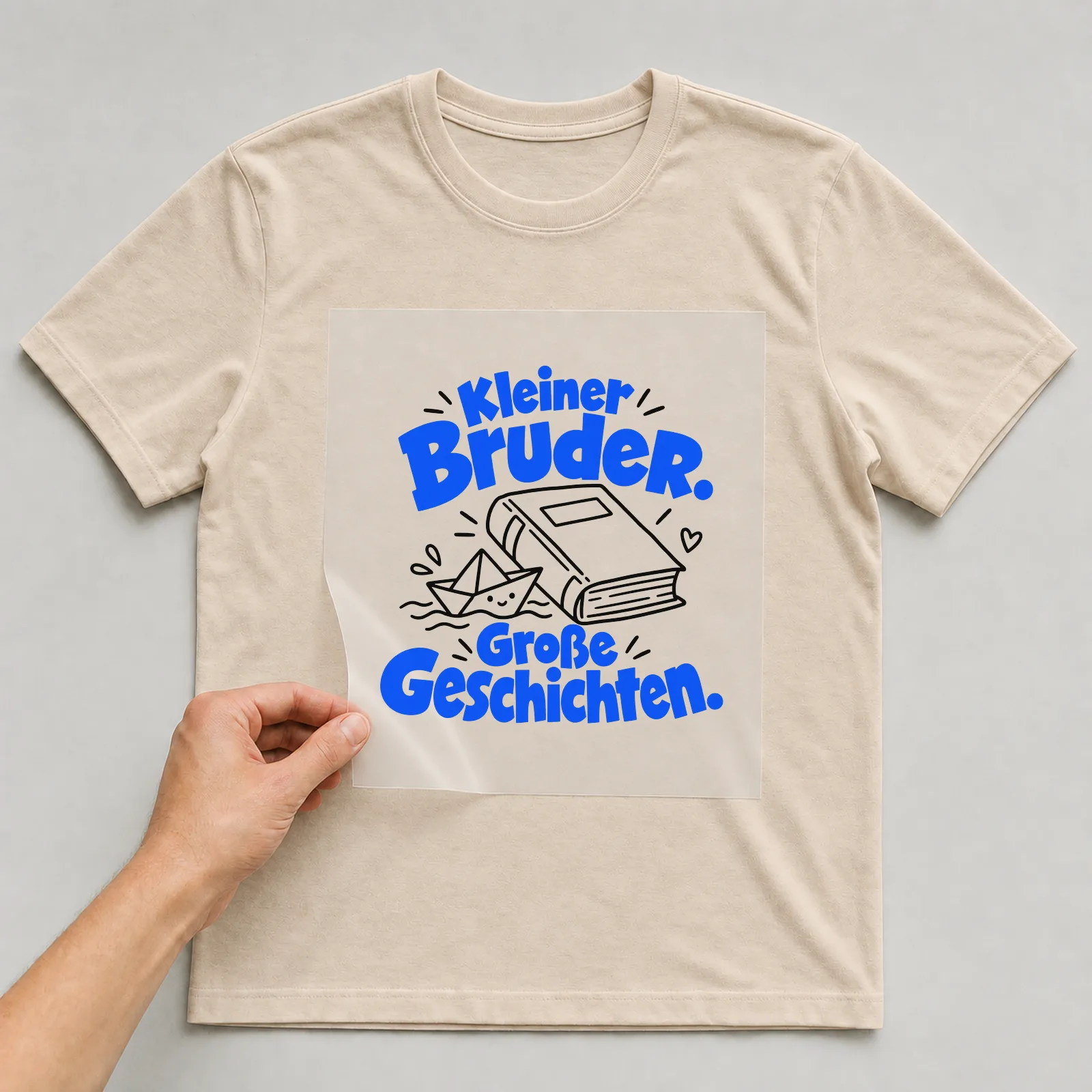 Bügelbild „Kleiner Bruder. Große Geschichten.“ auf beigem T-Shirt, Folie wird aufgelegt