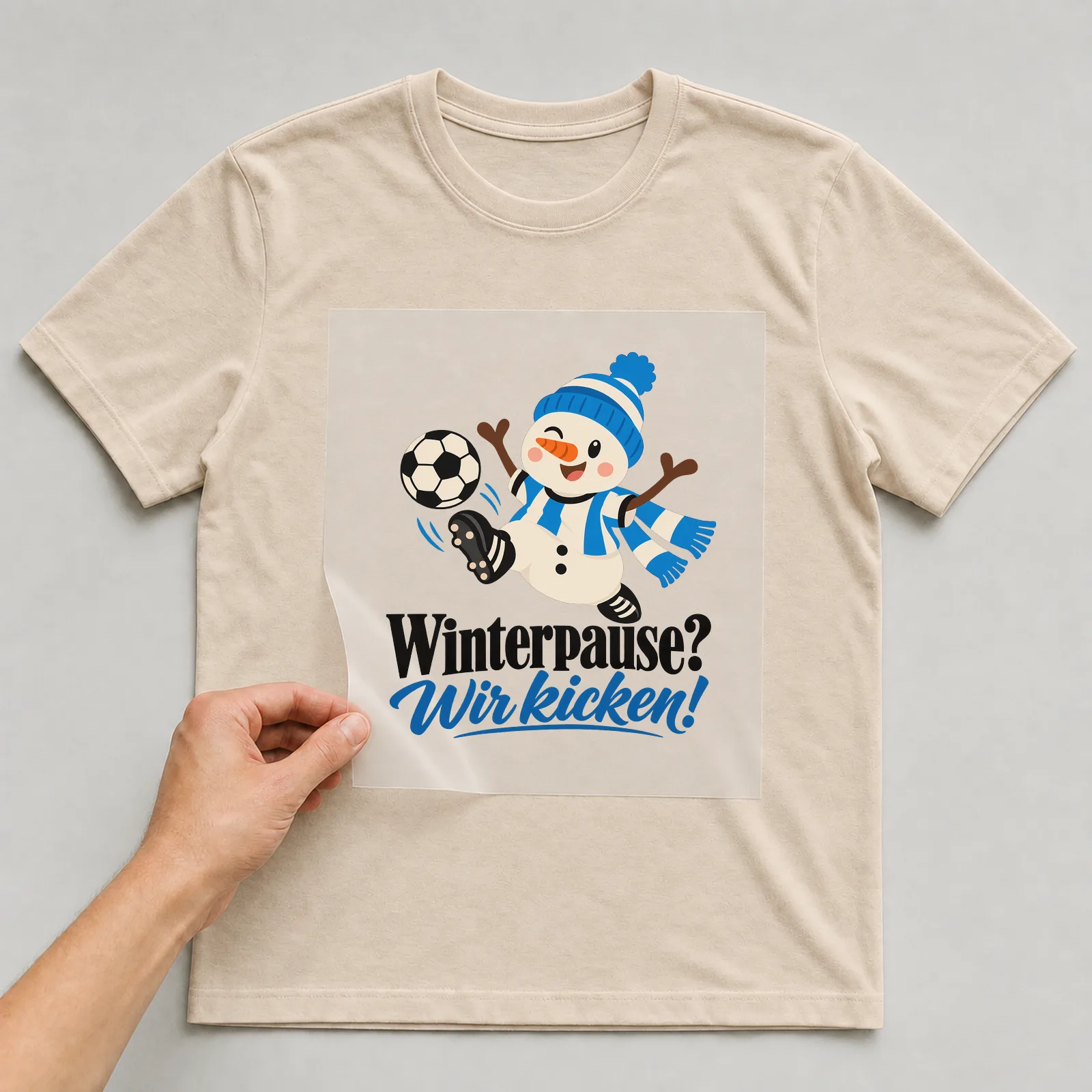 Bügelbild „Winterpause? Wir kicken!“ auf beigem T-Shirt, Folie wird aufgelegt