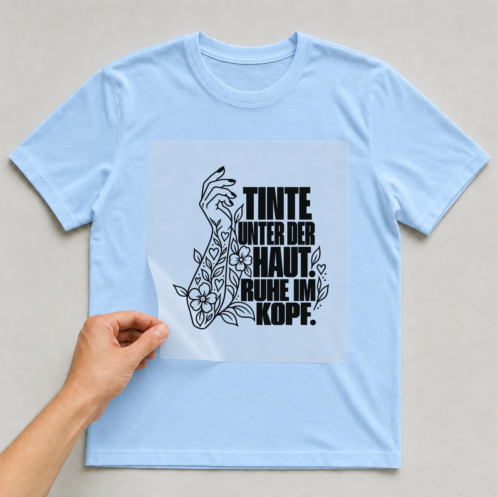 Bügelbild „Tinte unter der haut. Ruhe im Kopf.“ auf hellblauem T-Shirt, Folie wird aufgelegt