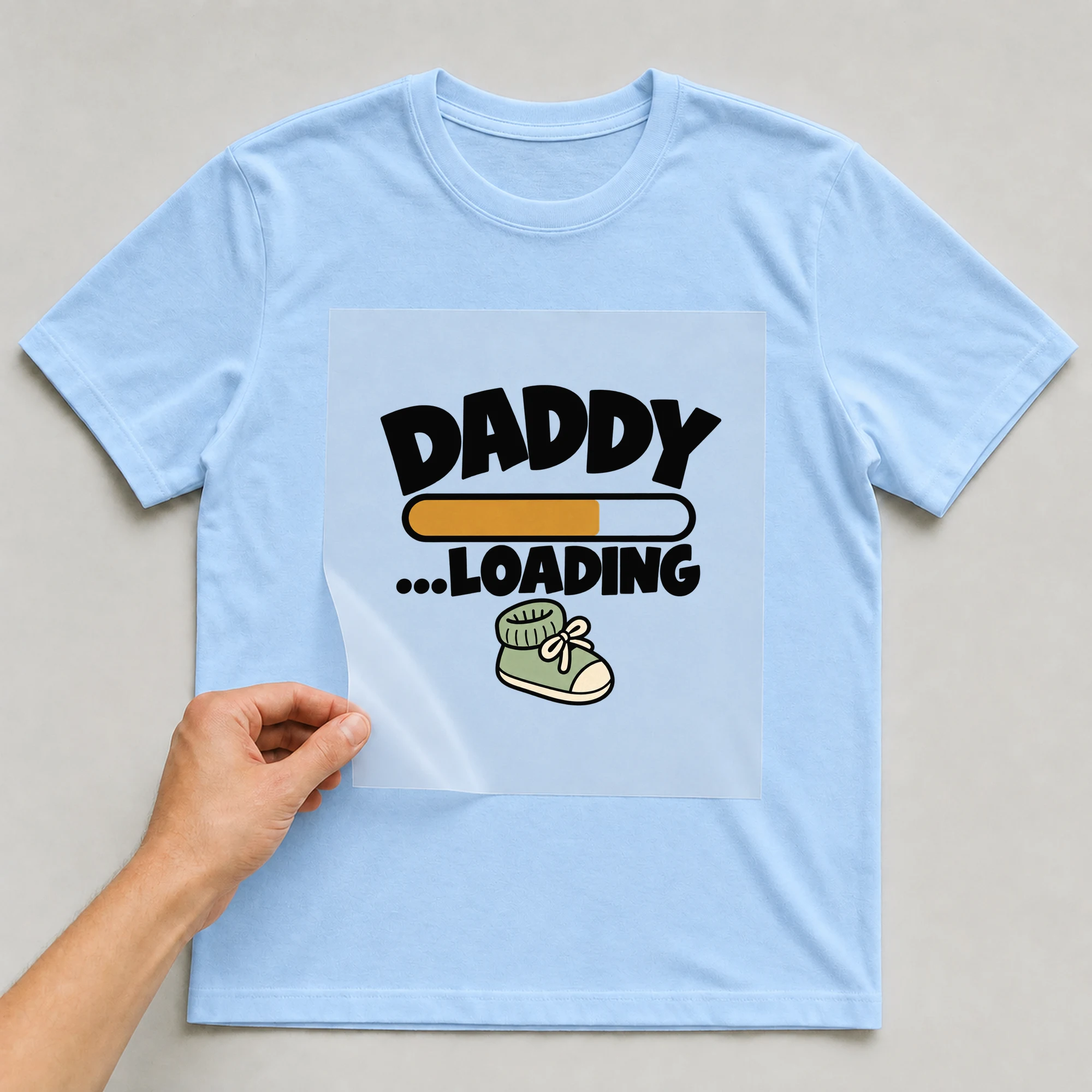 Bügelbild „Daddy ...loading“ auf babyblauem T-Shirt, Folie wird aufgelegt