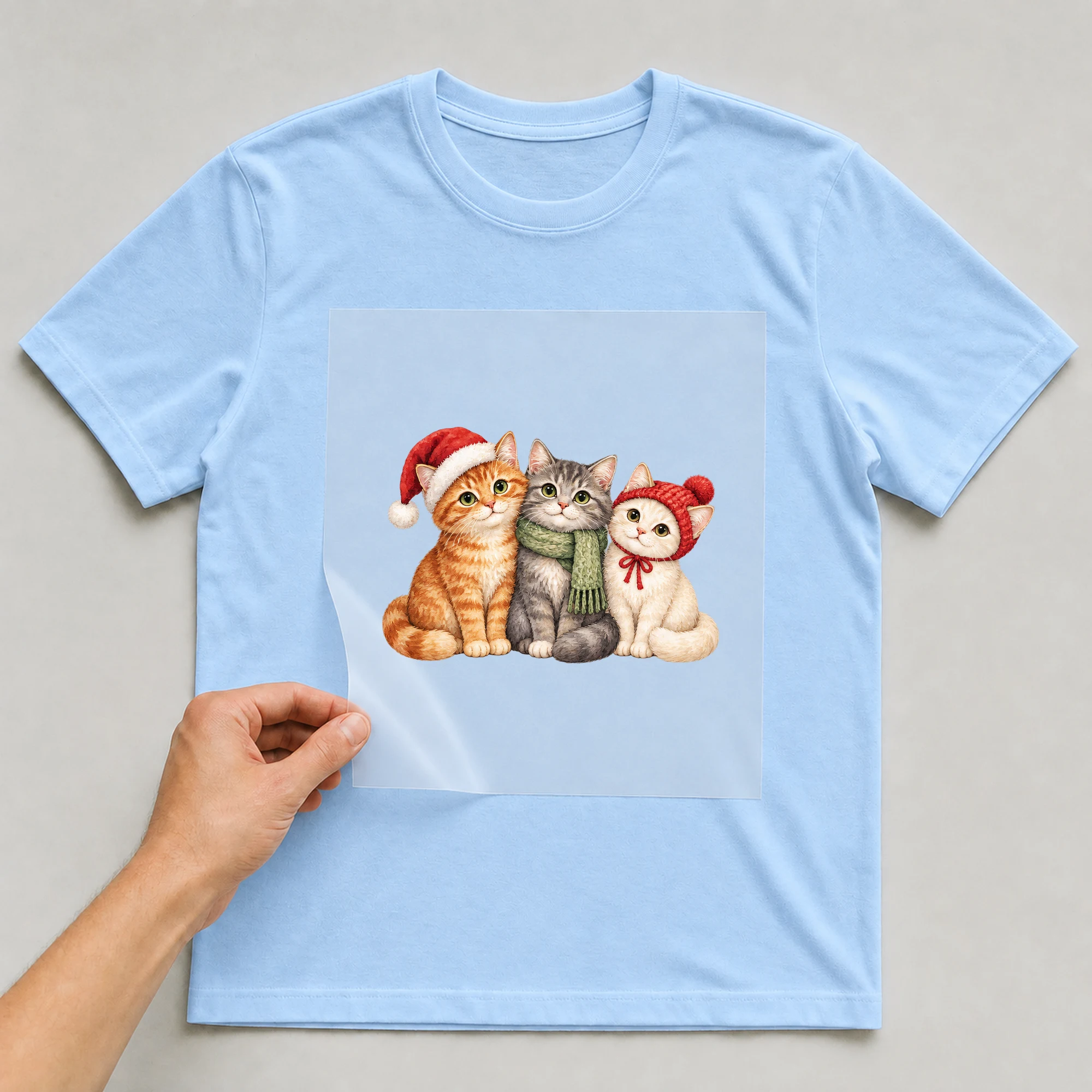 Bügelbild „Christmas Cats“ auf babyblauem T-Shirt, Folie wird aufgelegt