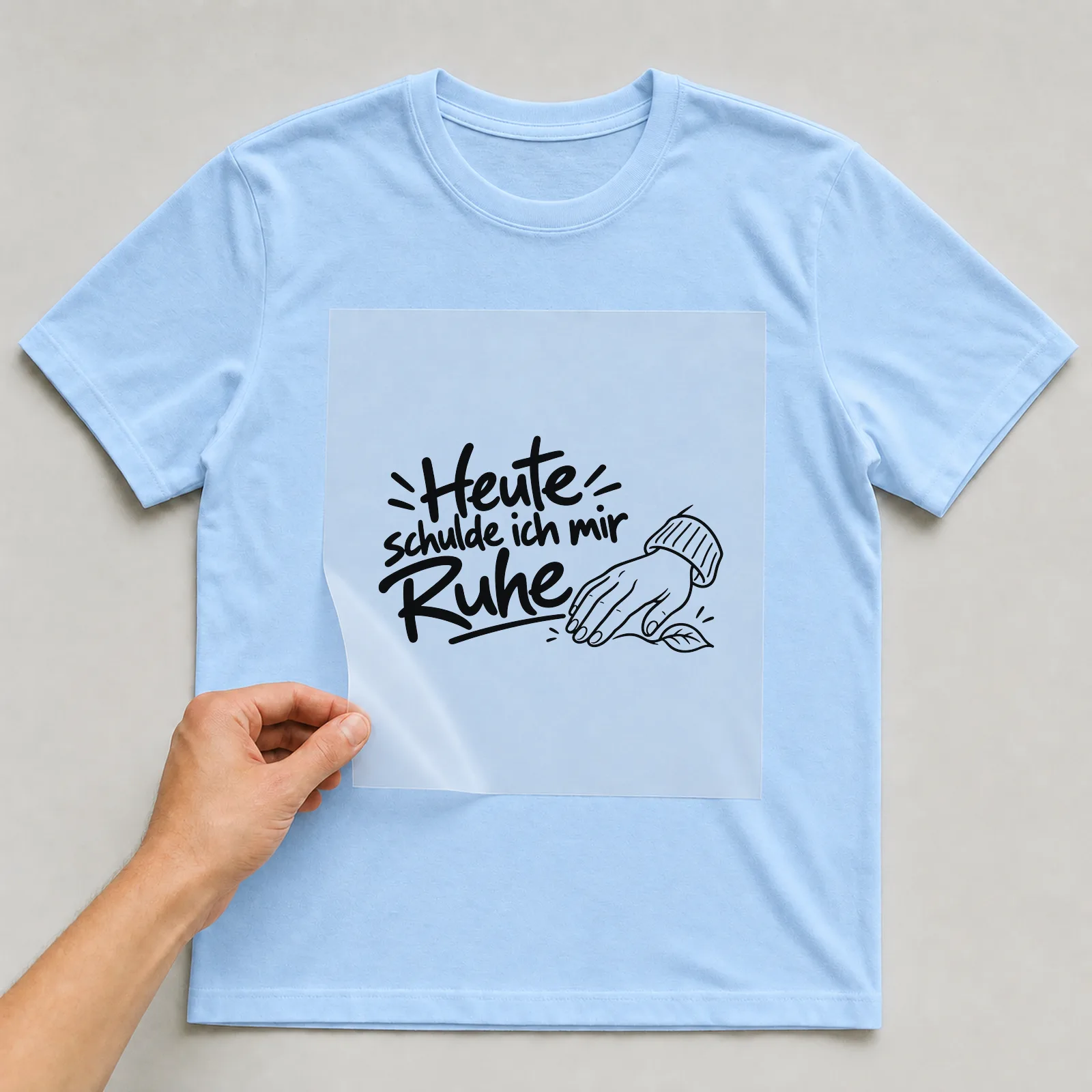 Bügelbild „Heute schulde ich mir Ruhe“ auf hellblauem T-Shirt, Folie wird aufgelegt