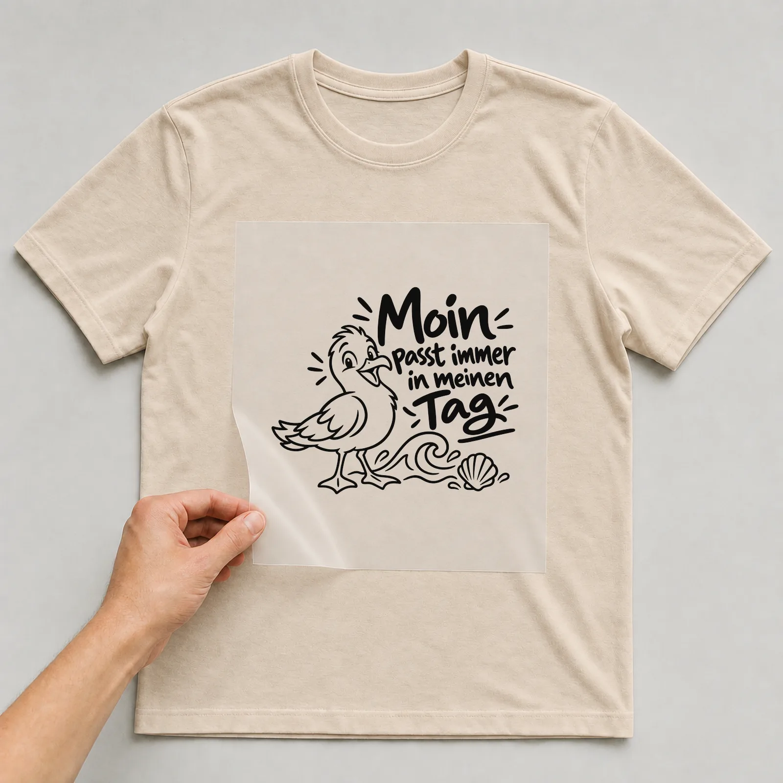 Bügelbild „Moin passt immer in meinen Tag“ auf beigem T-Shirt, Folie wird aufgelegt