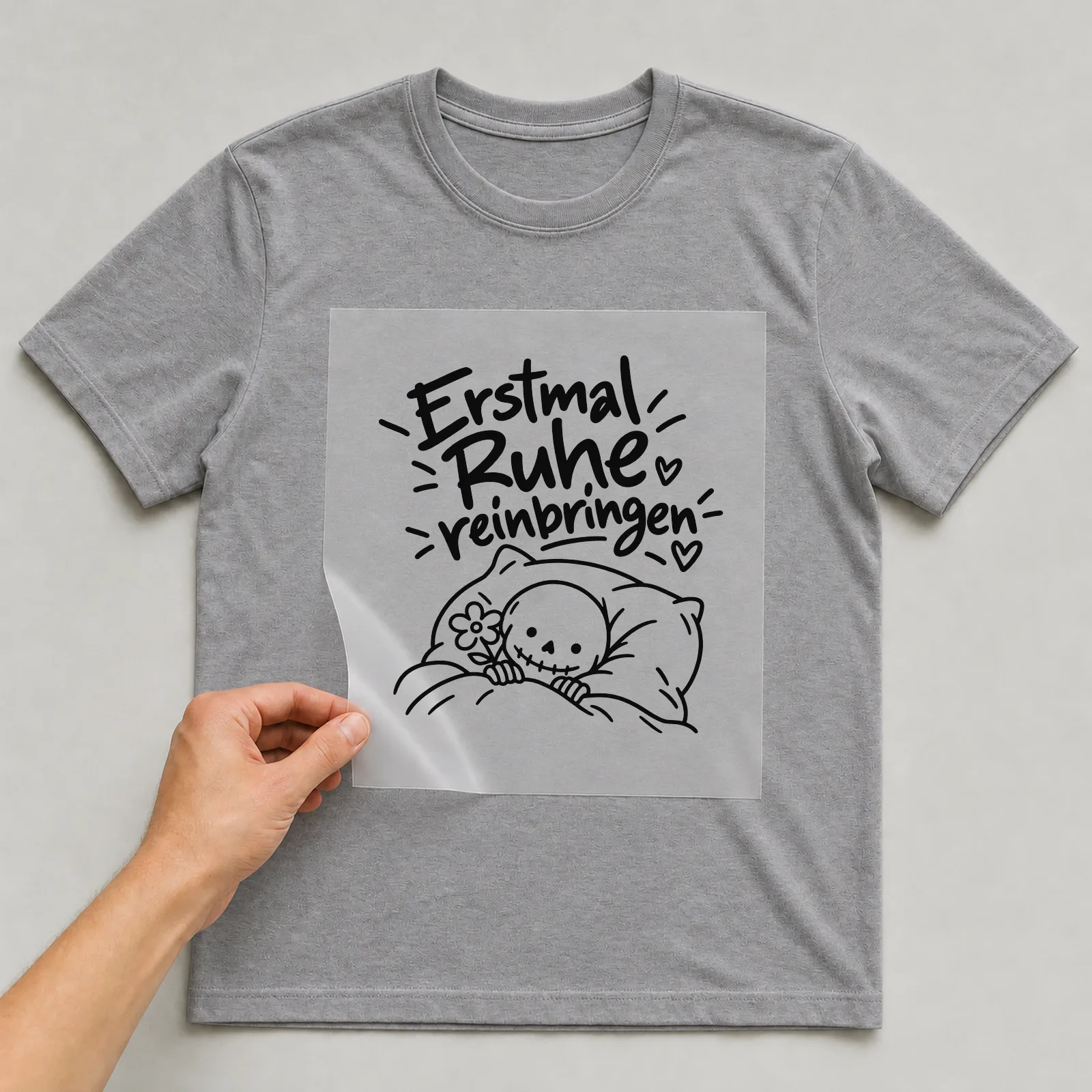 Bügelbild „Erstmal Ruhe reinbringen“ auf grauem T-Shirt, Folie wird aufgelegt