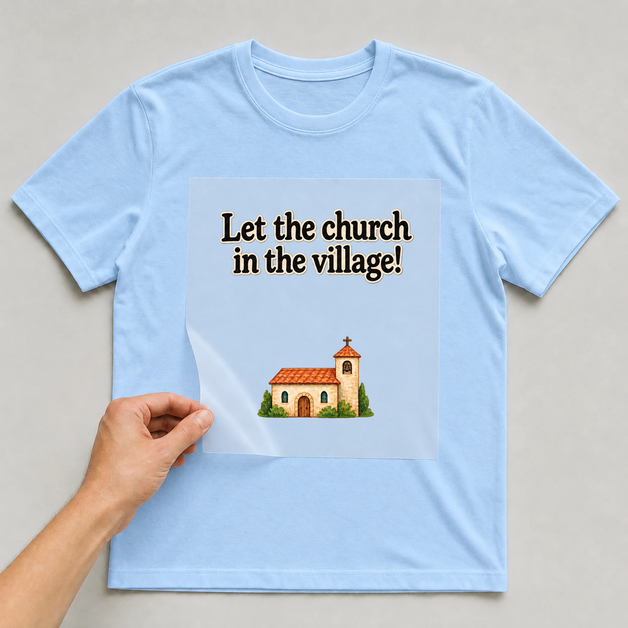 Bügelbild „Let the church in the village!“ auf babyblauem T-Shirt, Folie wird aufgelegt