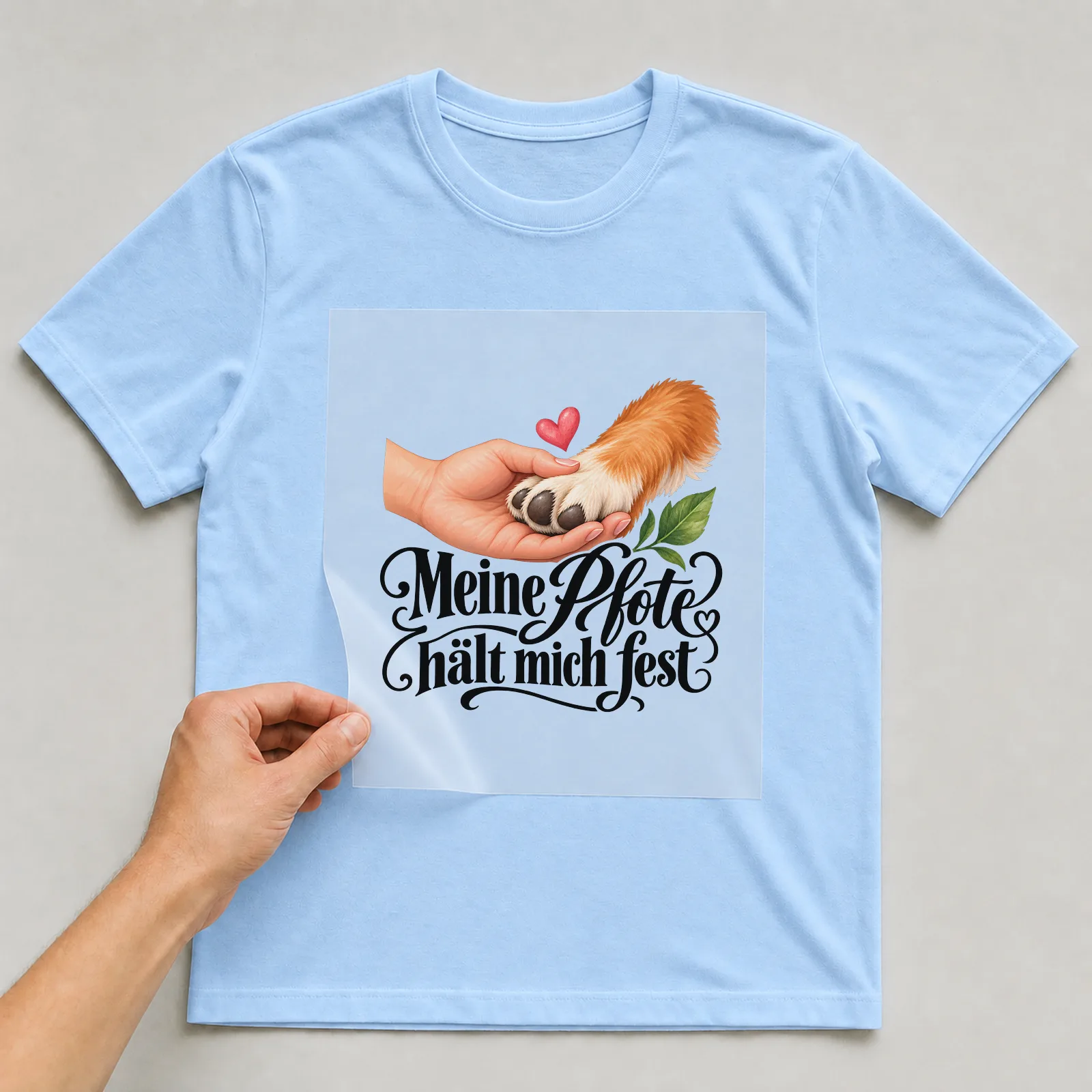 Bügelbild „Meine Pfote hält mich fest“ auf hellblauem T-Shirt, Folie wird aufgelegt