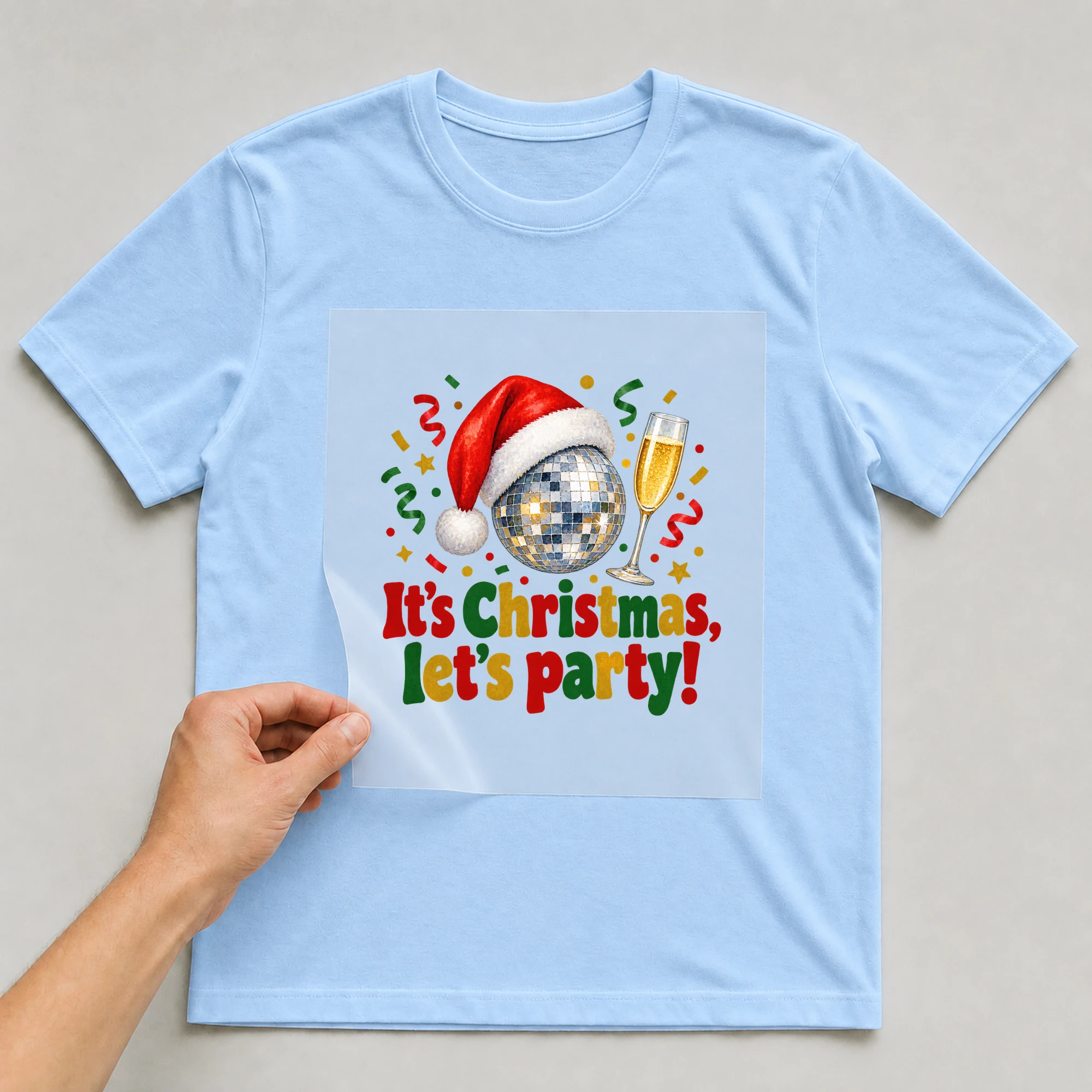 Bügelbild „It's Christmas, let's party!“ auf babyblauem T-Shirt, Folie wird aufgelegt
