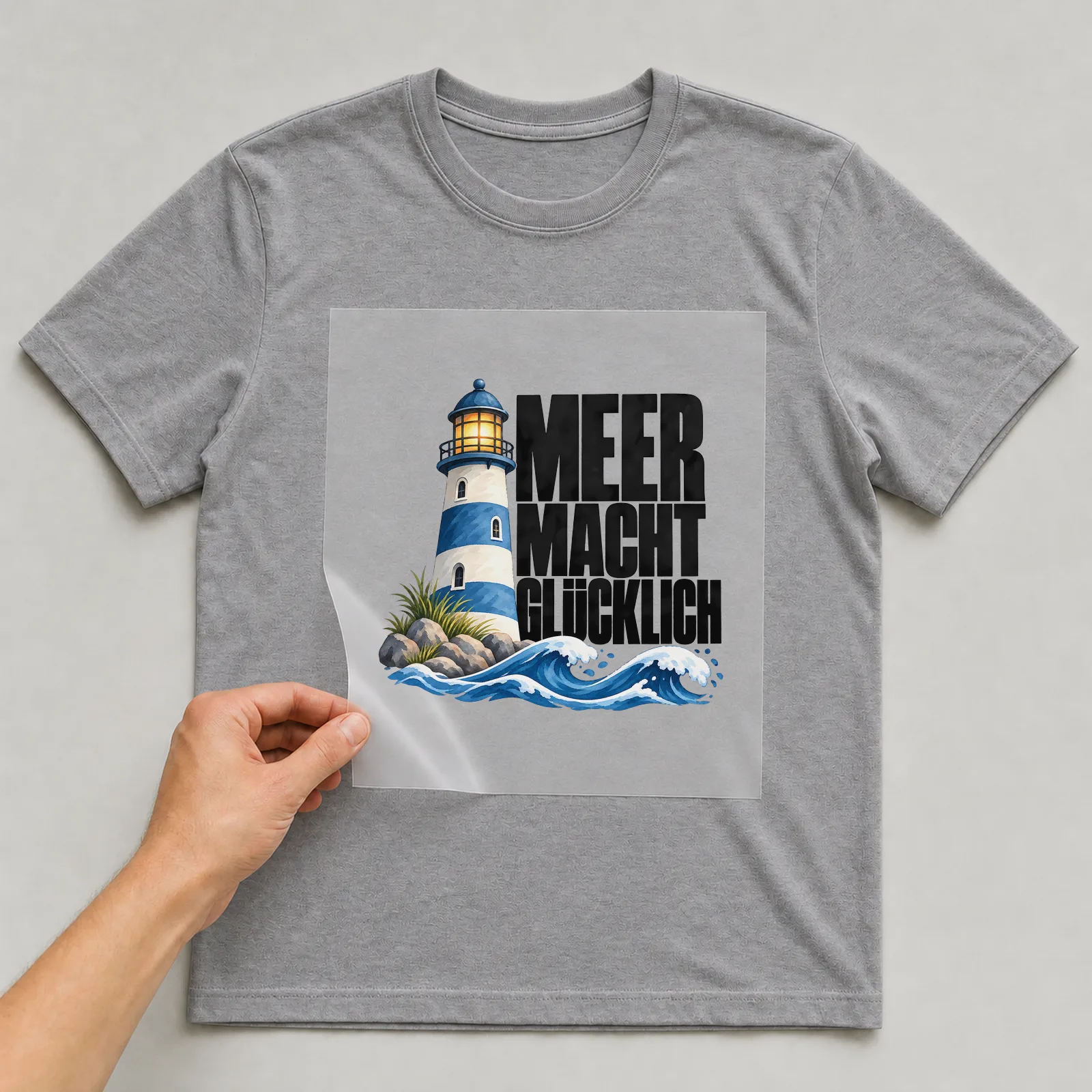Bügelbild „Meer macht glücklich“ auf grauem T-Shirt, Folie wird aufgelegt