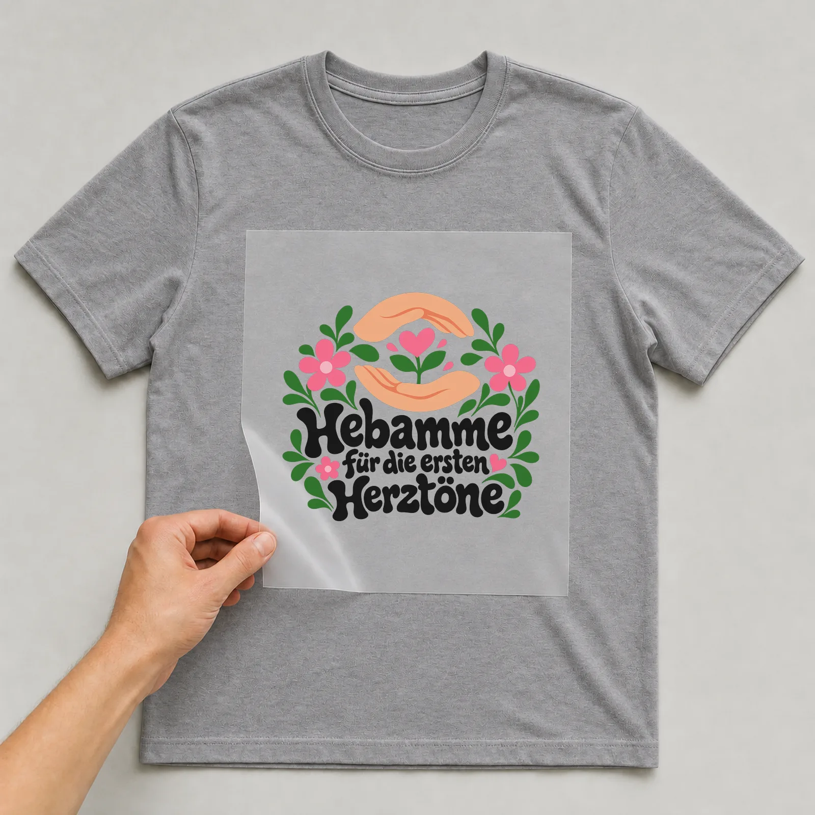 Bügelbild „Hebamme für die ersten Herztöne“ auf grauem T-Shirt, Folie wird aufgelegt