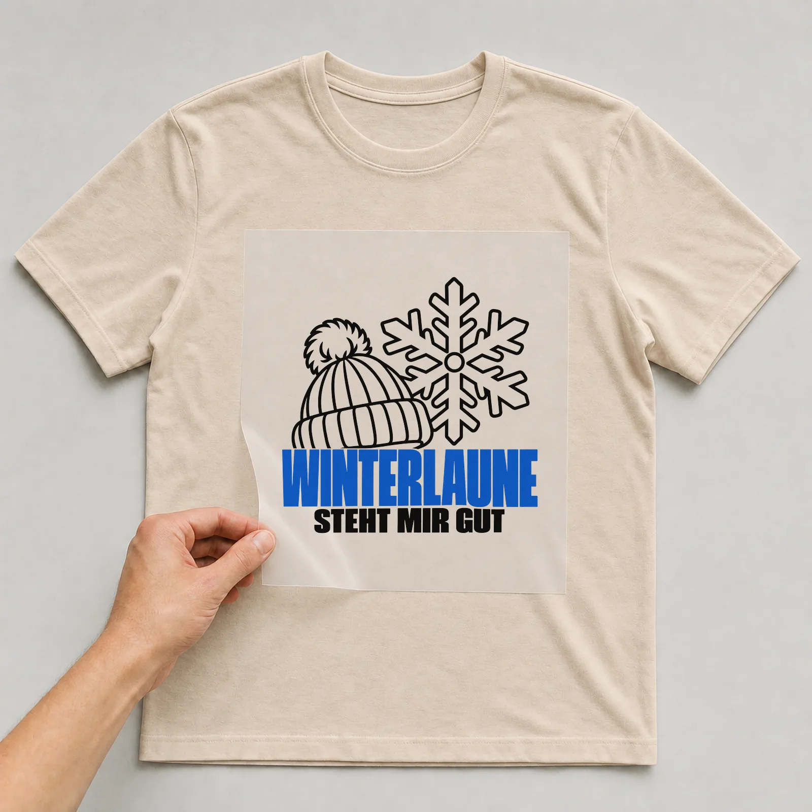 Bügelbild „Winterlaune steht mir gut“ auf beigem T-Shirt, Folie wird aufgelegt