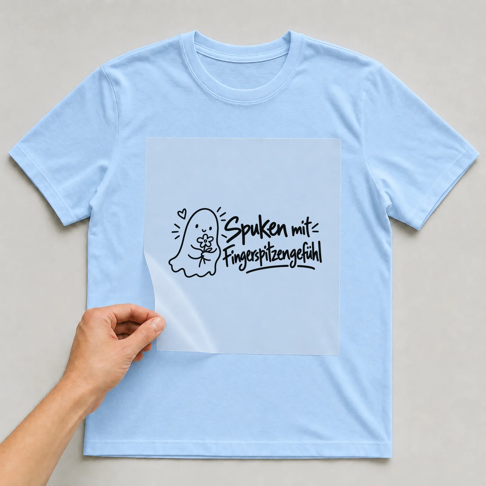 Bügelbild „Spuken mit Fingerspitzengefühl“ auf hellblauem T-Shirt, Folie wird aufgelegt