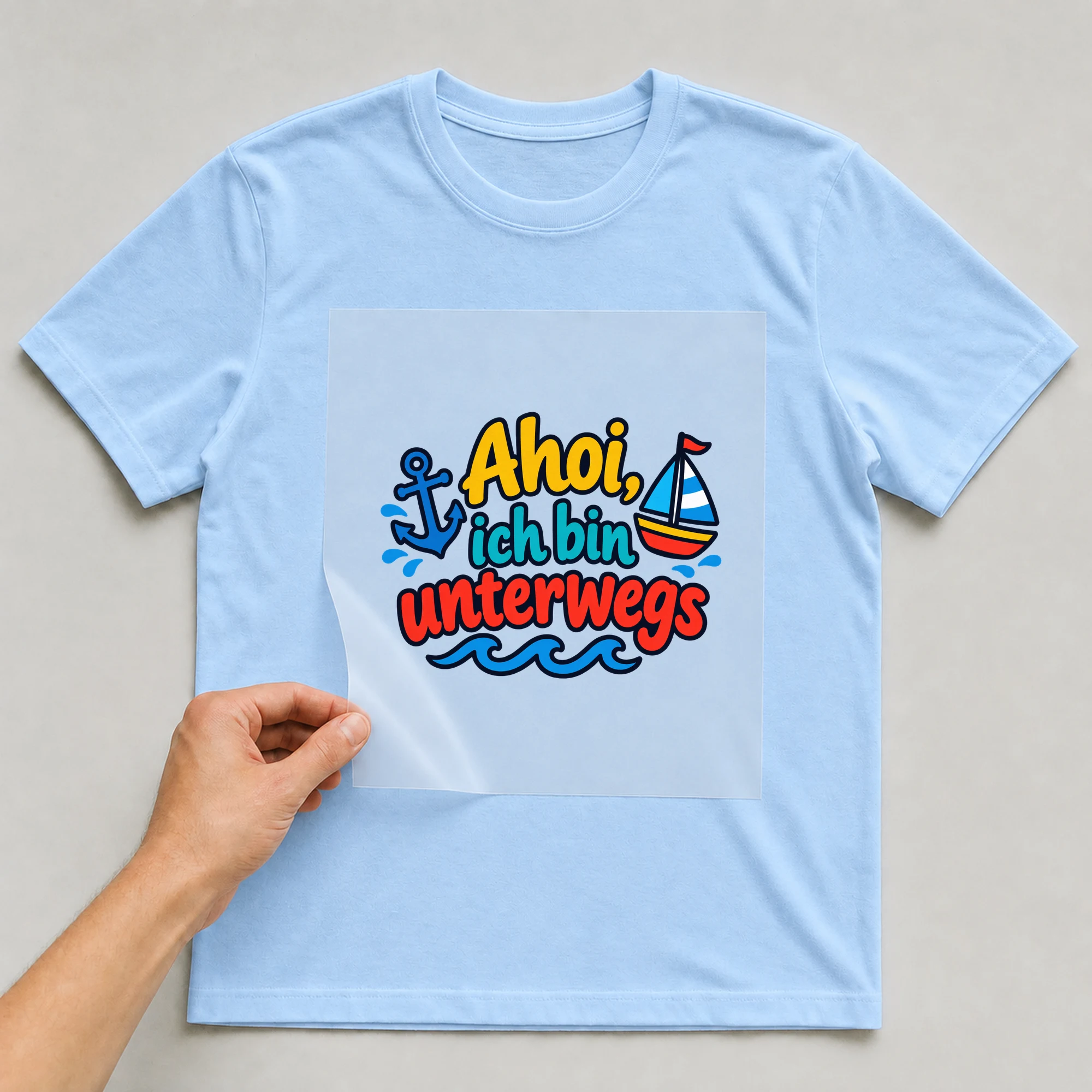 Bügelbild „Ahoi, ich bin unterwegs“ auf babyblauem T-Shirt, Folie wird aufgelegt