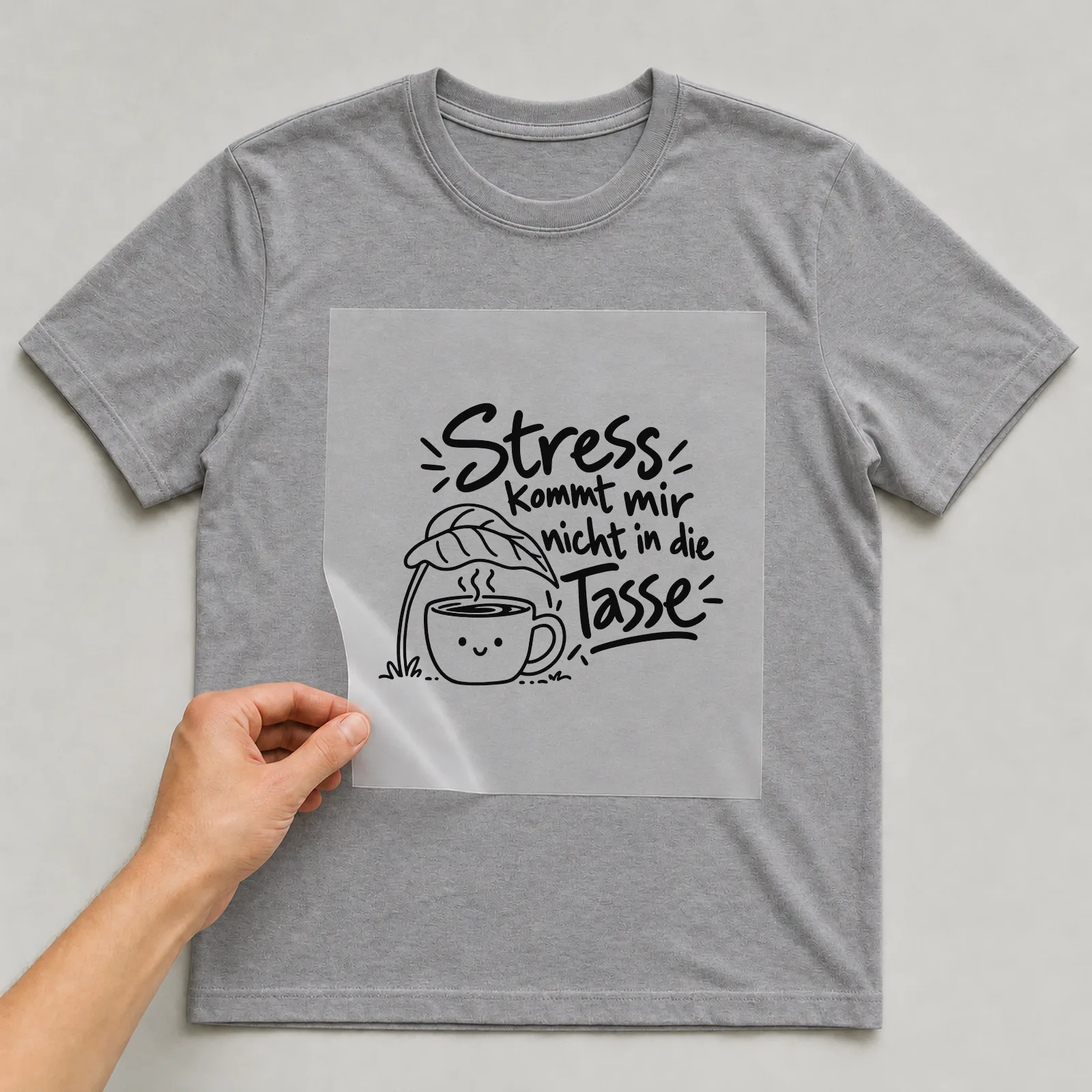 Bügelbild „Stress kommt mir nicht in die Tasse“ auf grauem T-Shirt, Folie wird aufgelegt